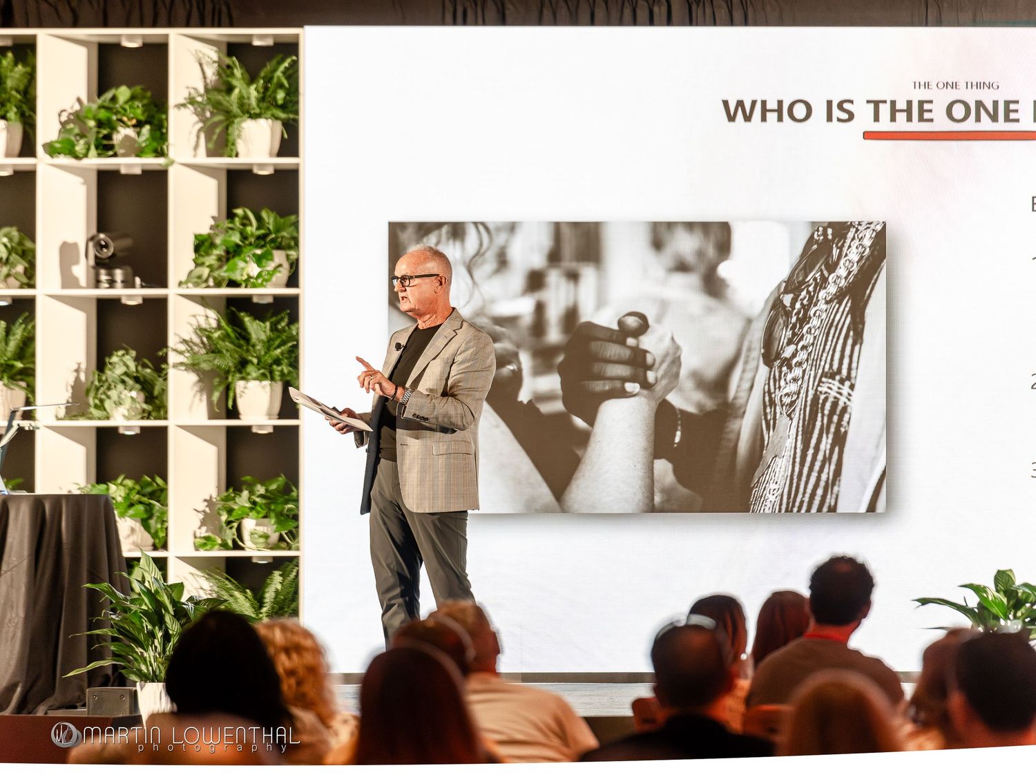 Corporate speaker presenting to a seated audience during a professional event.