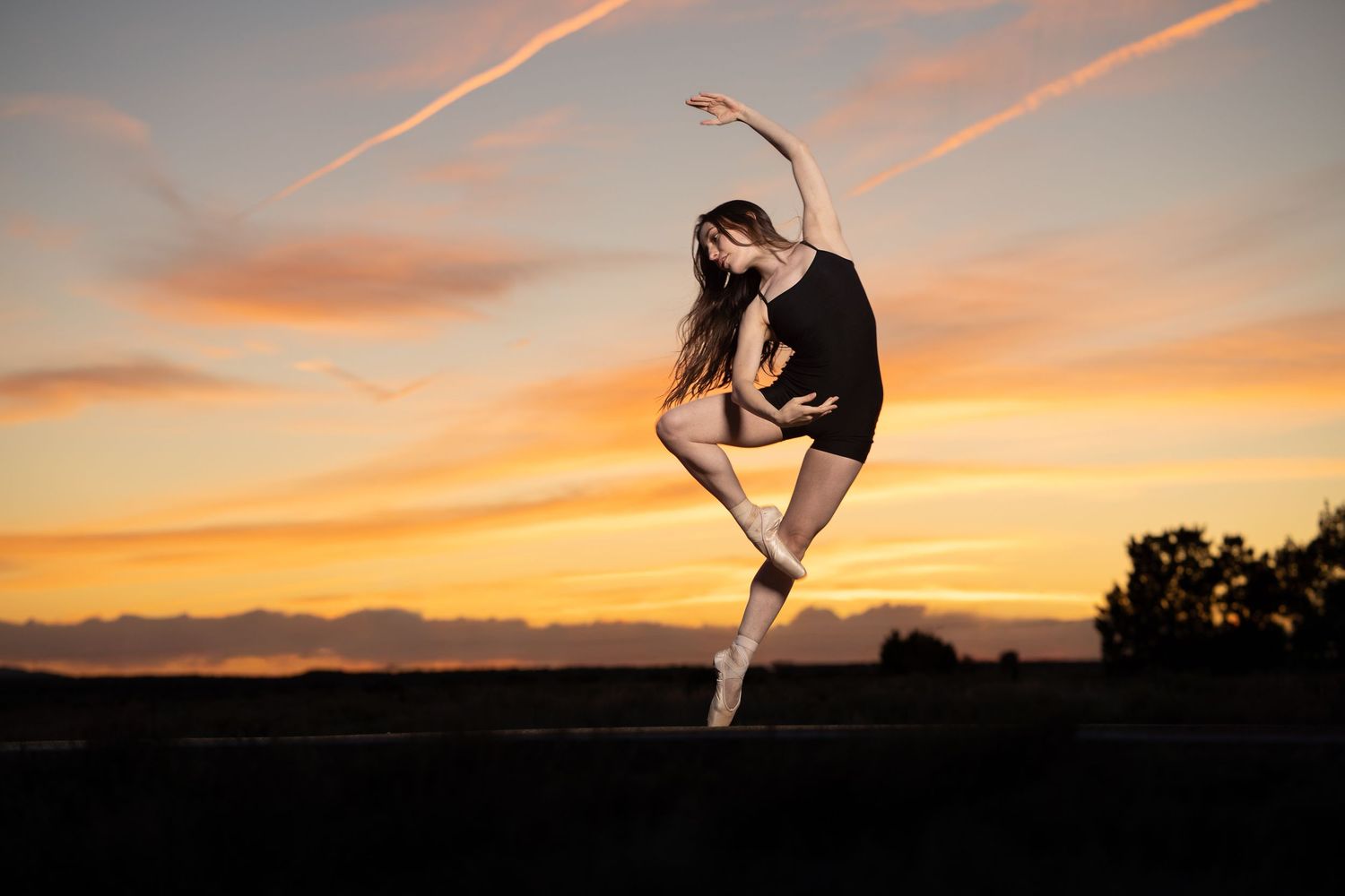 Dancer captured in a graceful pose against a sunset sky.