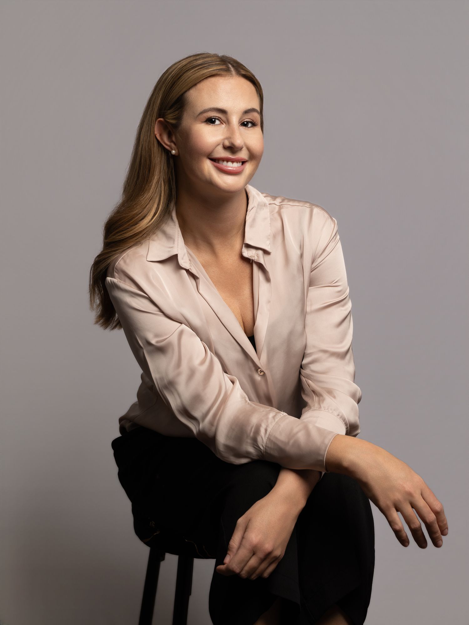 Professional woman in a beige blouse seated against a neutral studio backdrop.