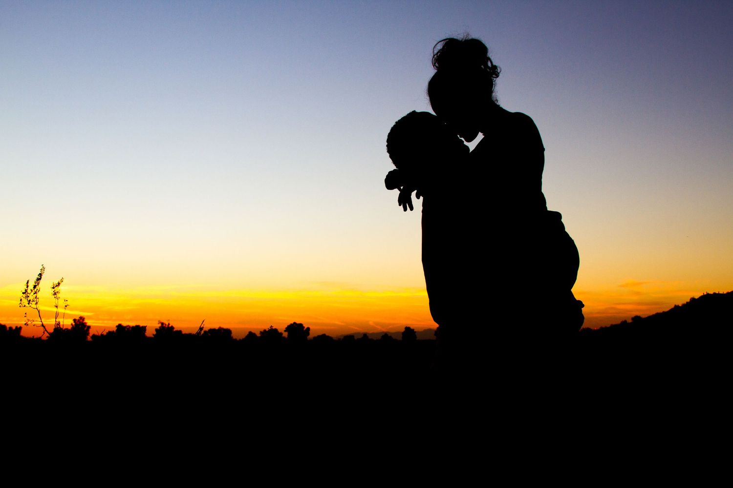 Silhouette of a parent holding a child against a colorful sunset sky.