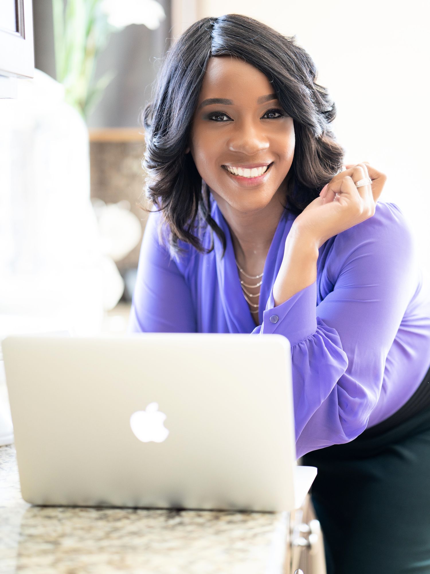 Smiling professional in a purple blouse working at a laptop.
