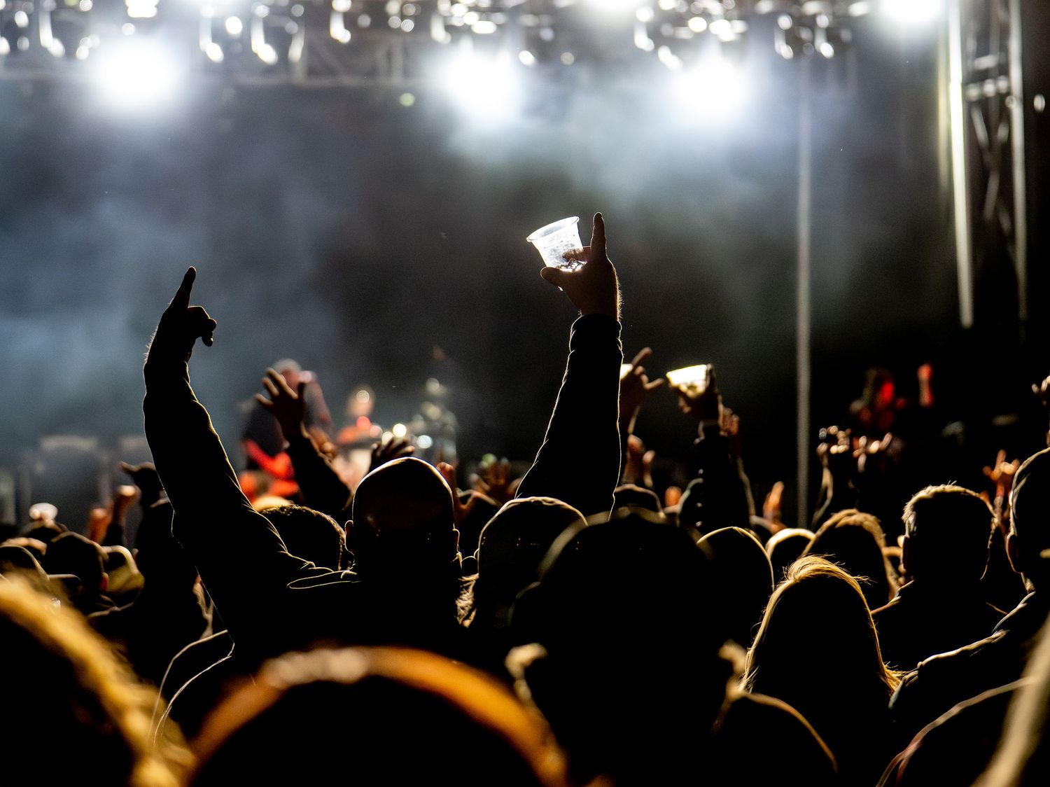 Concert crowd raising phones and hands beneath bright stage lights.