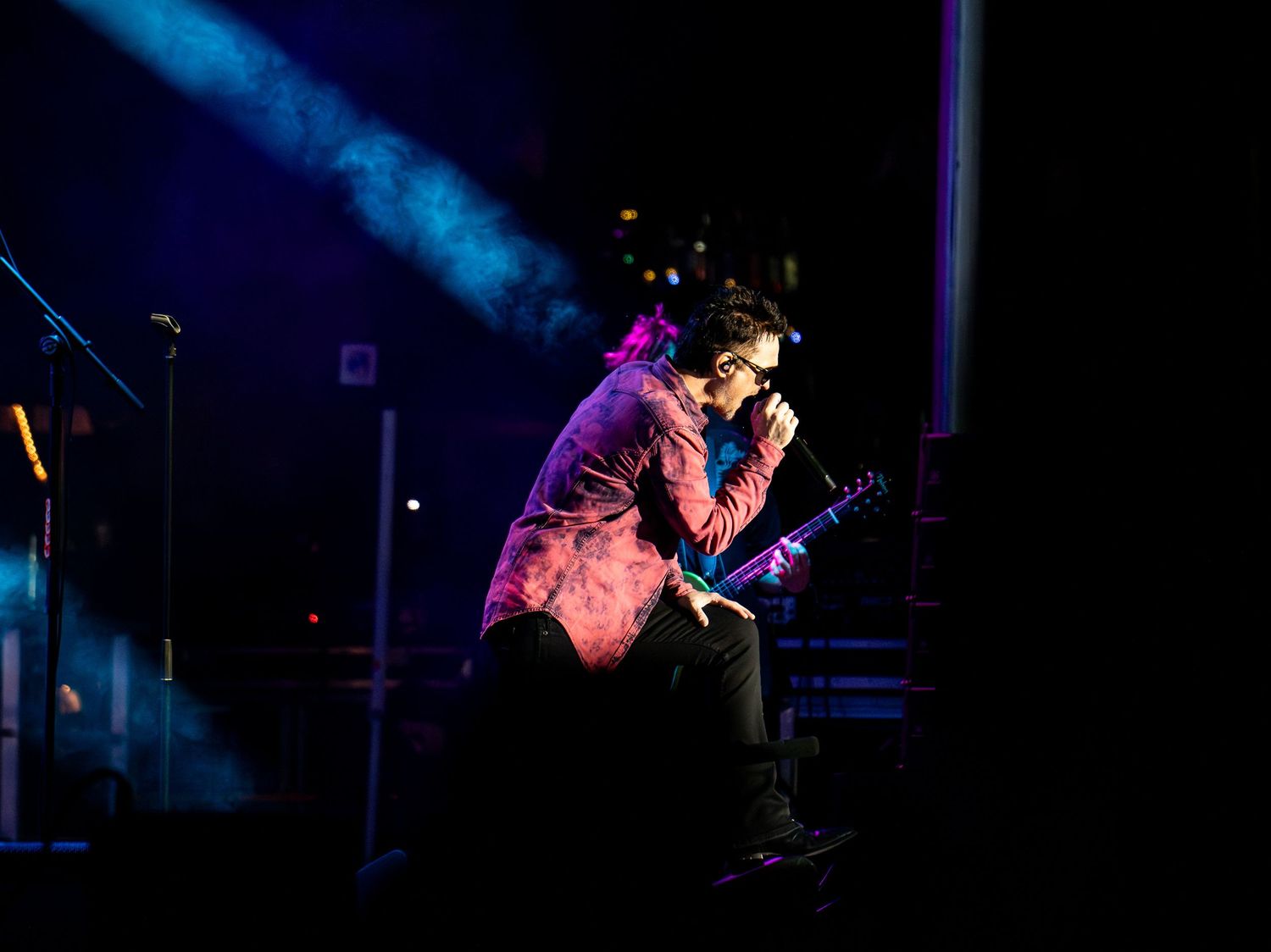 Singer performing onstage beneath blue and purple concert lighting.