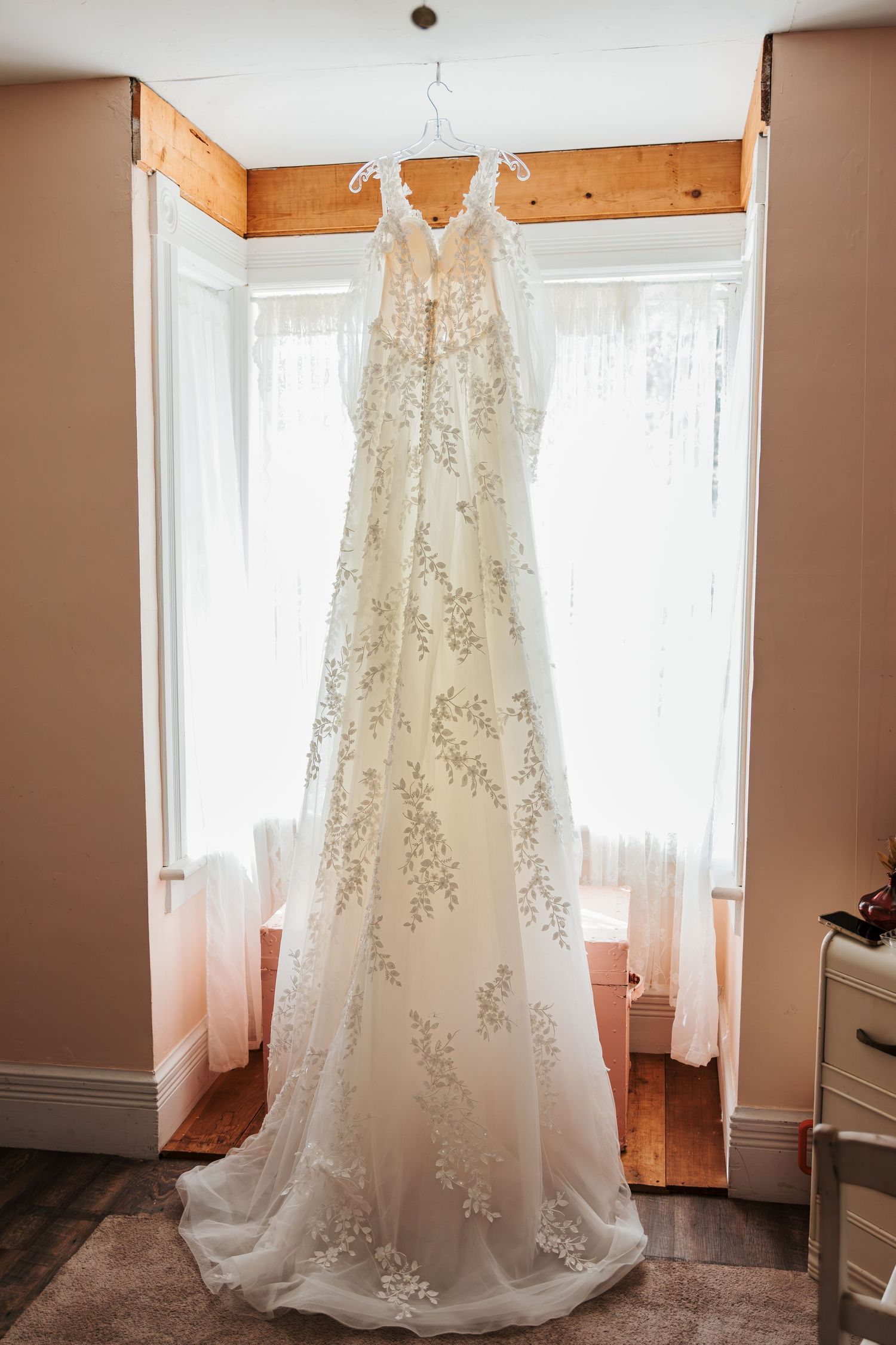 Elegant white lace wedding gown with floral embroidery hanging in a sunlit window before the ceremony. Langley BC wedding at golf course