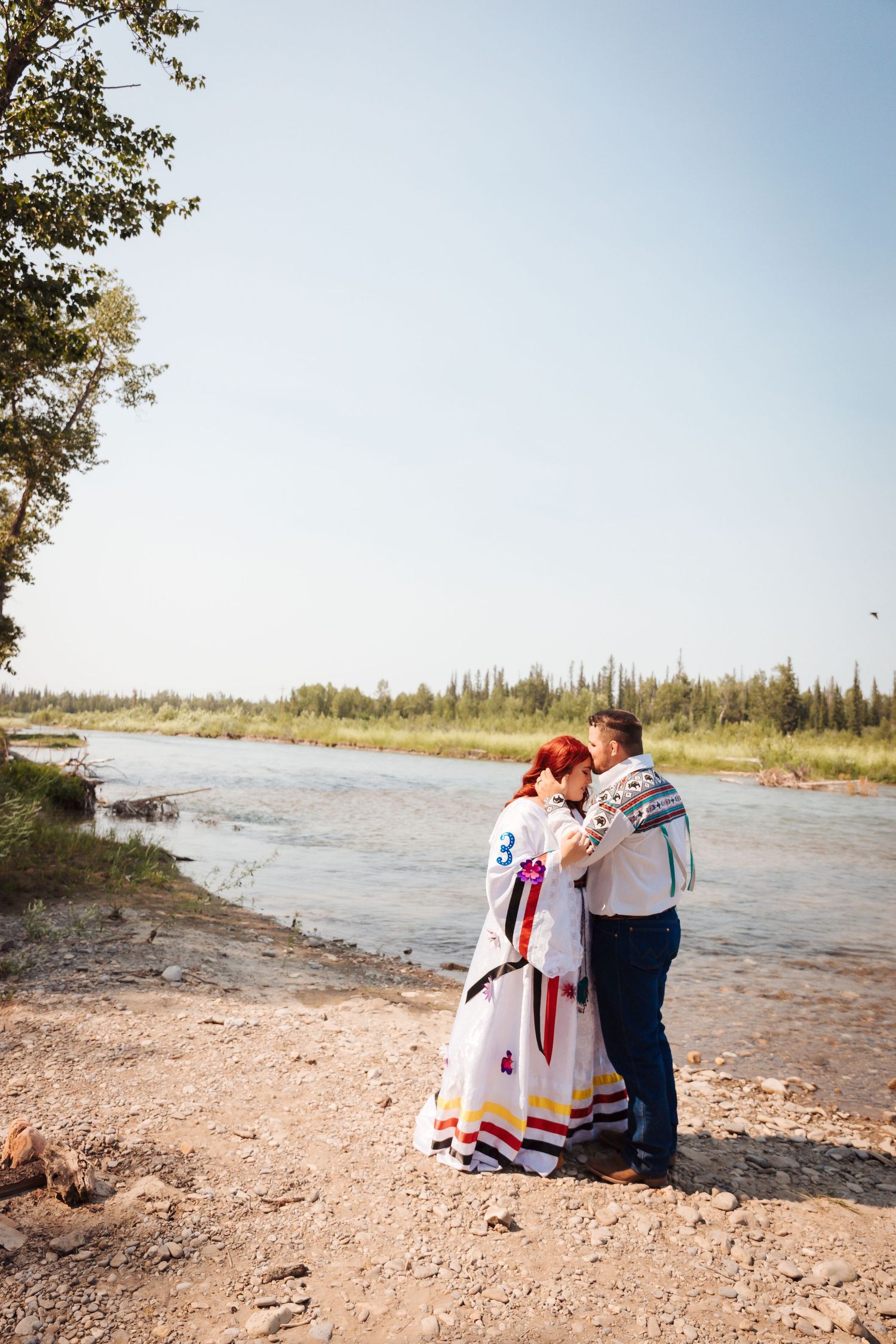 Country wedding decor. Metis wedding dresses. Calgary lifestyle wedding photographers. bride and groom holding each other infront of a river