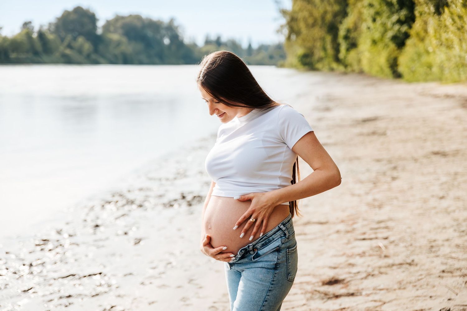 maternity photoshoot by a river. Pregnancy pictures. Mother with pregnant belly in jean and tshirt. Family and newborn photographers