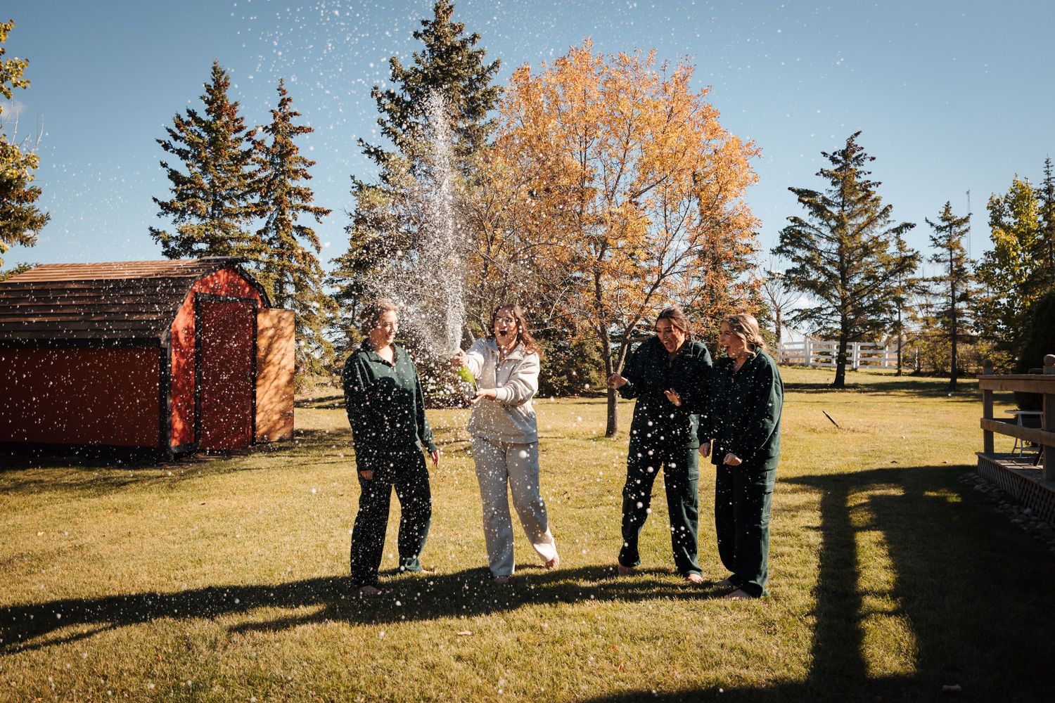 Four people celebrating outdoors on a sunny fall day with confetti and champagne on a green lawn.