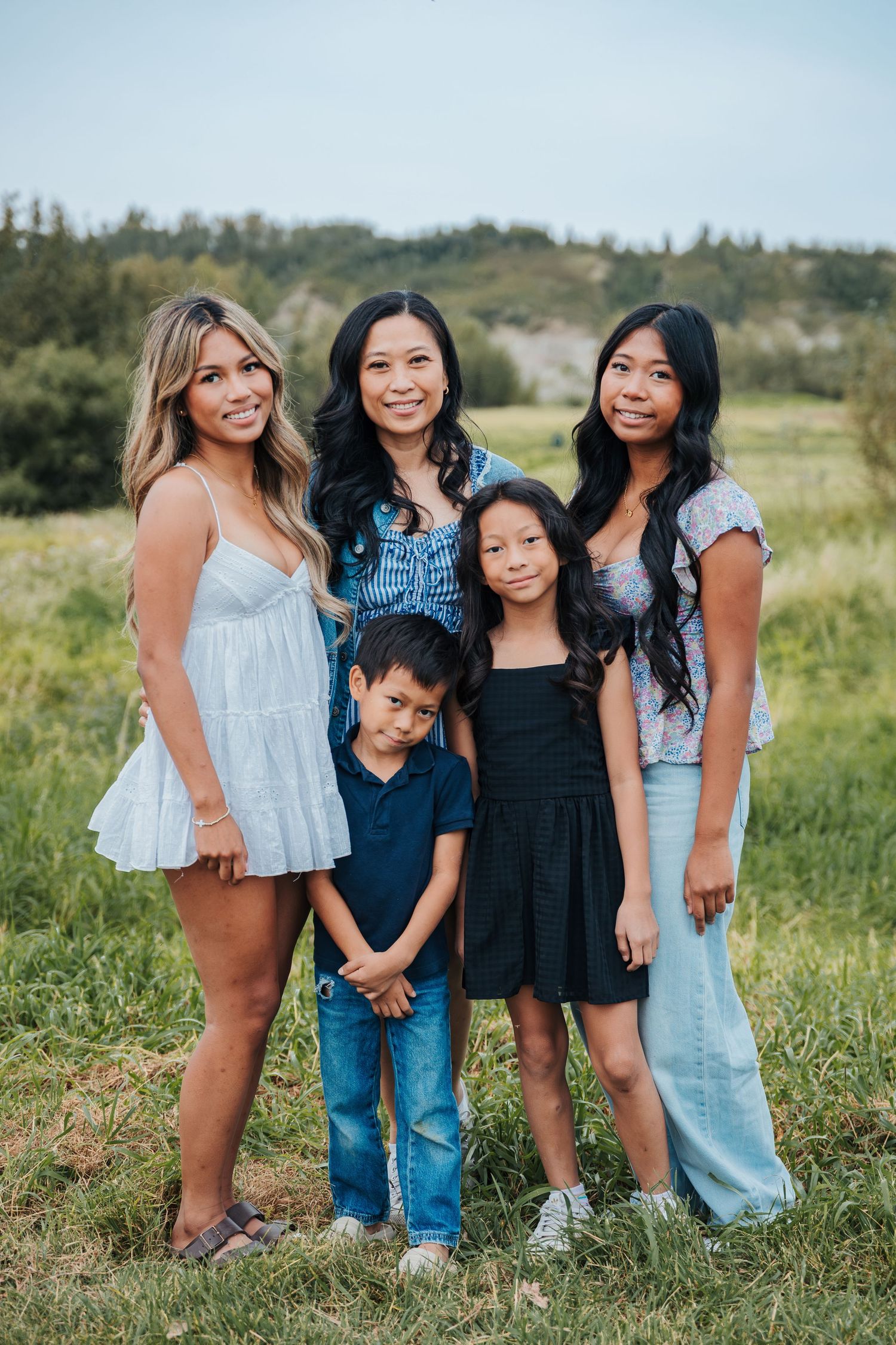 A family of five poses outdoors in a green field, including three girls, a boy, and a woman smiling together. Edmonton parks and trails