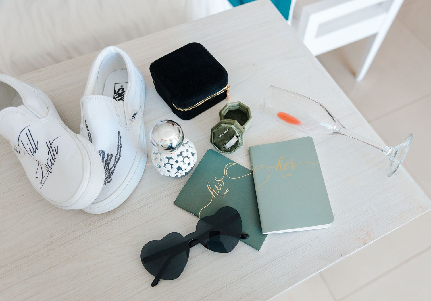 White Vans sneakers, sunglasses, green notebooks, watch, and accessories flatlay on a white table.