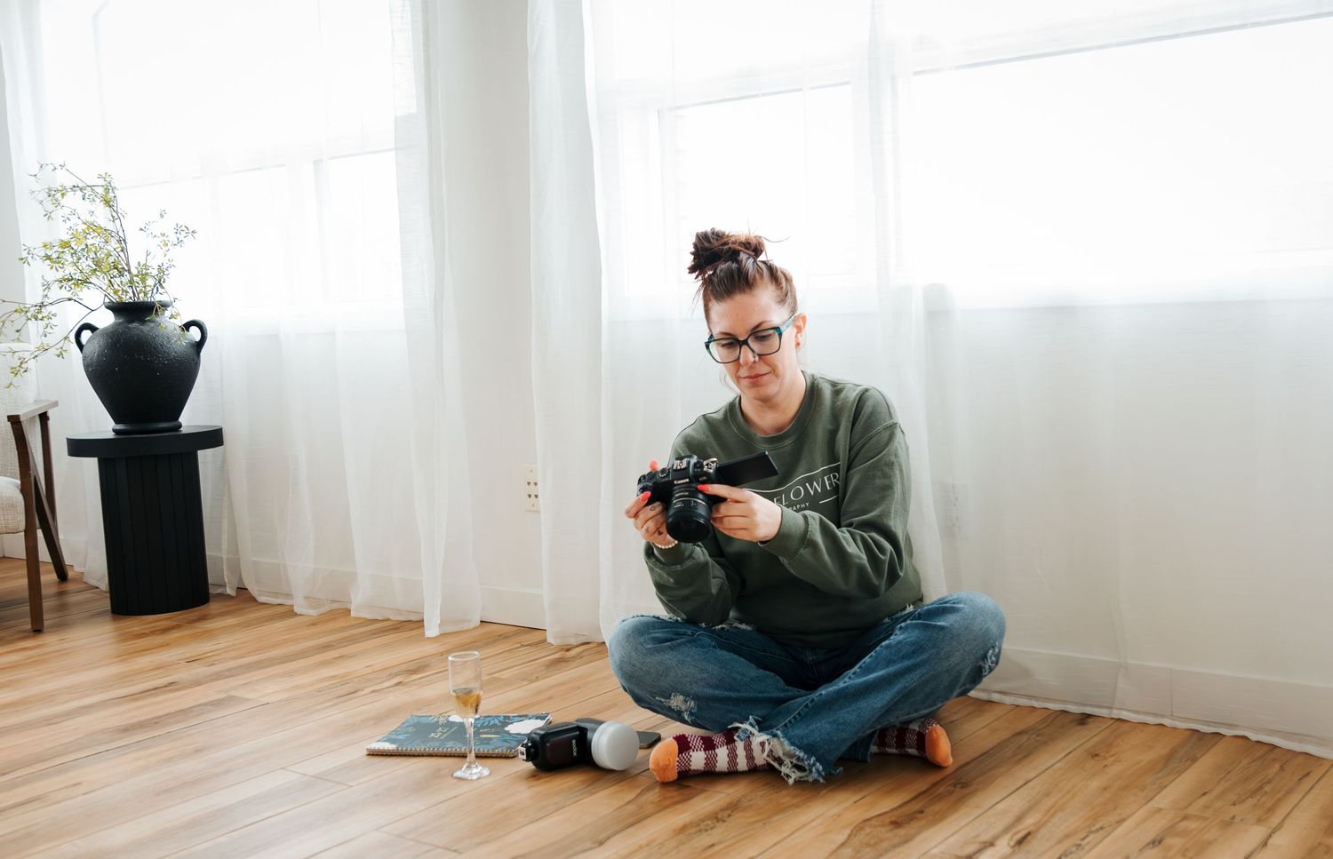 photographer sits with camera and champagne in a studio in St.Albert. Photography classes and mentorships. Ella mack creative. edmonton