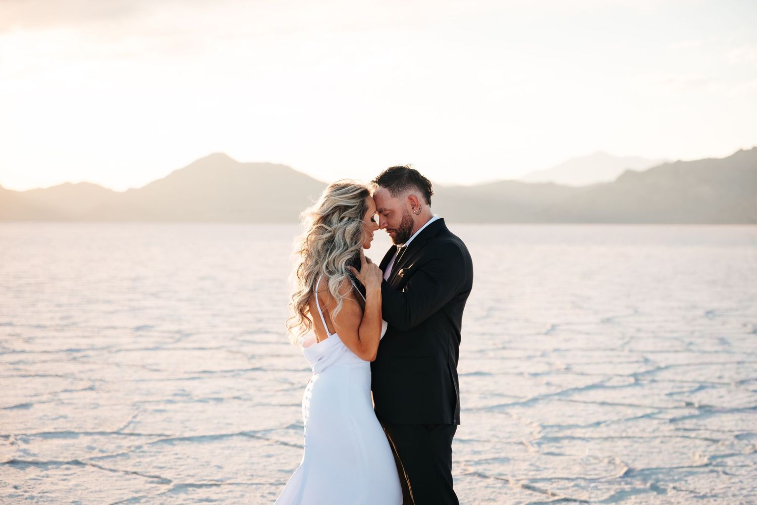 Bride and groom share a romantic moment at Bonneville Salt Flats with golden sunset and mountain backdrop. BC elopement photographer