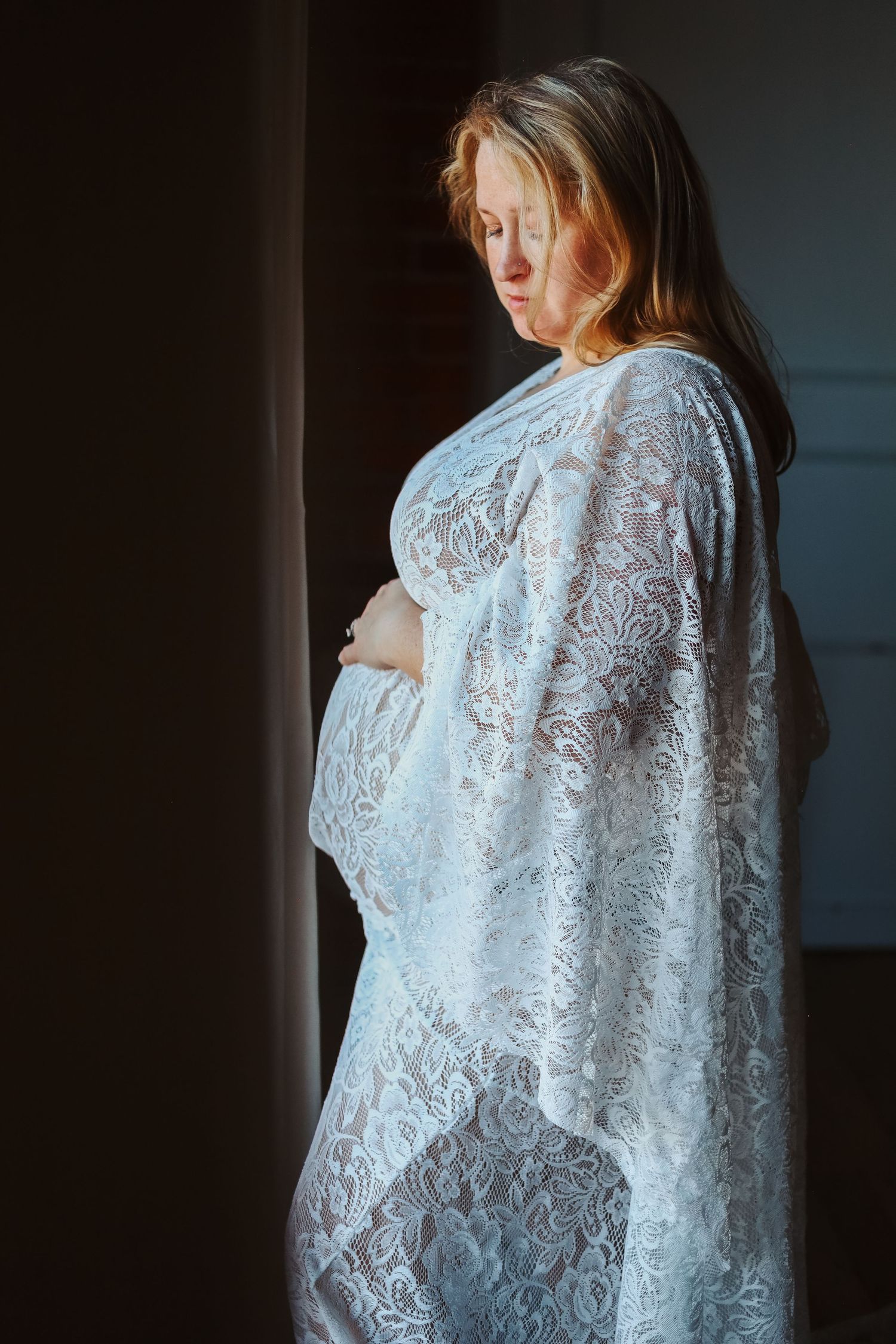 mom stands infront of window holding her pregnant belly for a maternity photoshoot. Edmonton and Stony Palin photographer. Family Pictures