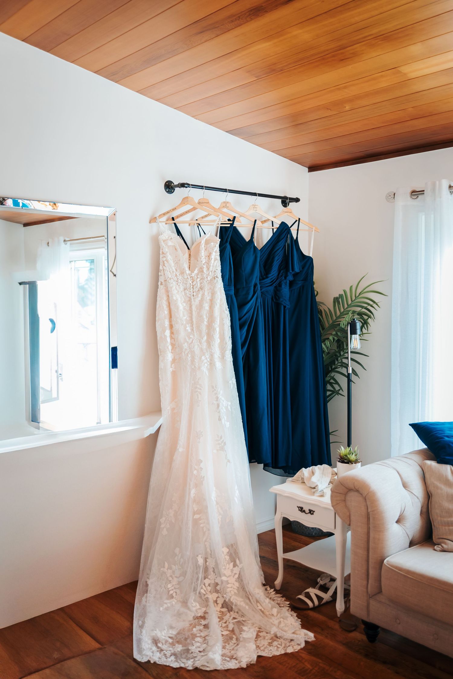 White lace wedding gown and navy blue bridesmaid dresses hanging in a bright bridal suite with wood ceiling.