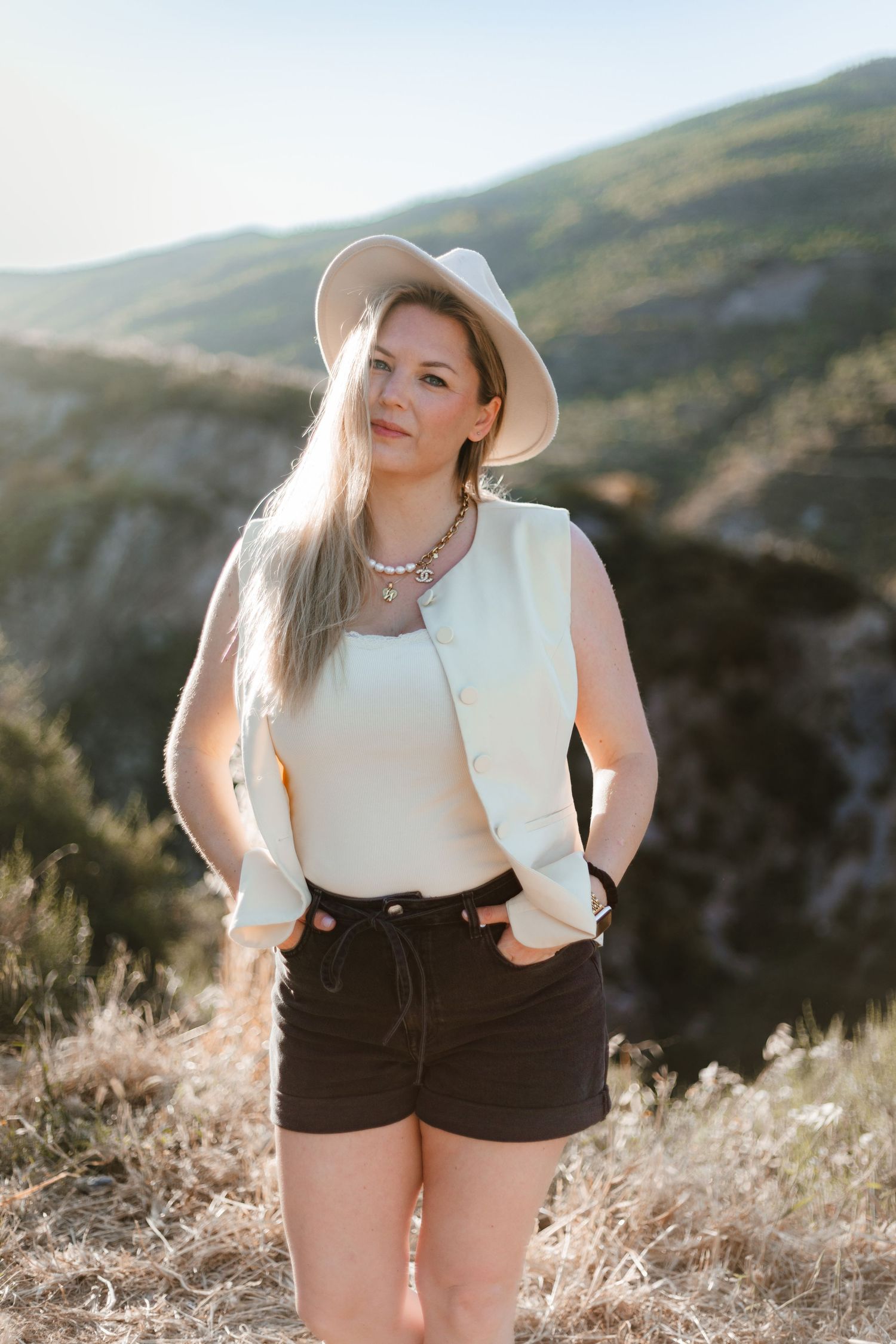 Woman in white hat and shorts posing in mountain landscape at golden hour.