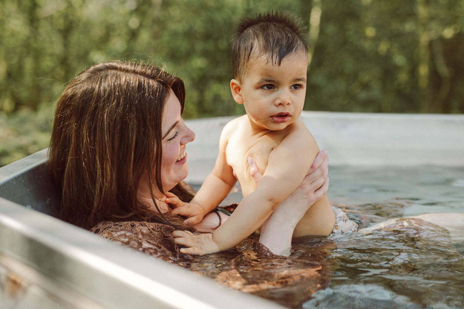 Mother and baby enjoying a relaxing outdoor bath together surrounded by lush green trees.