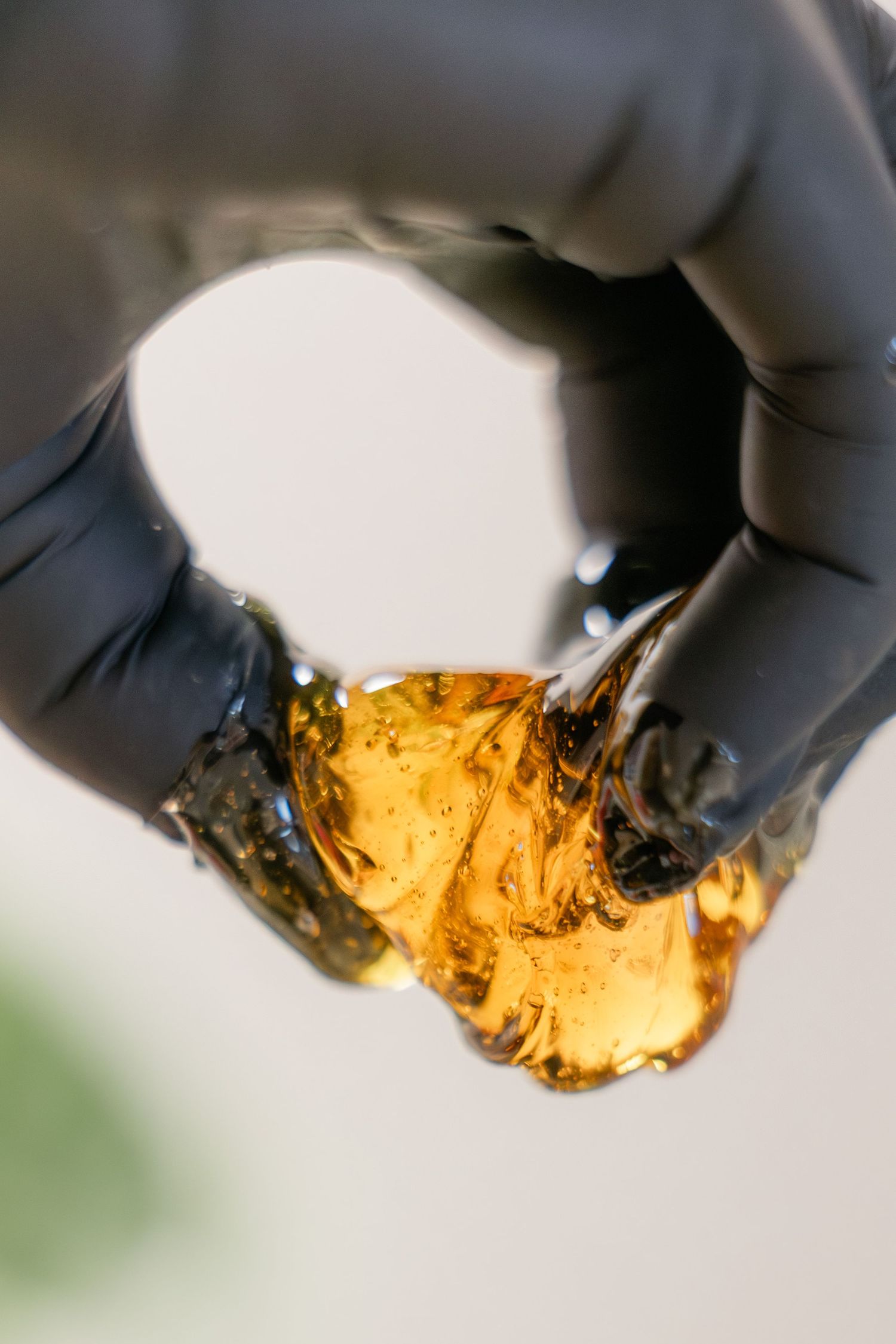 handen met handschoen met gouden amberkleurige sugarwax hars, met doorschijnende kleverige textuur.