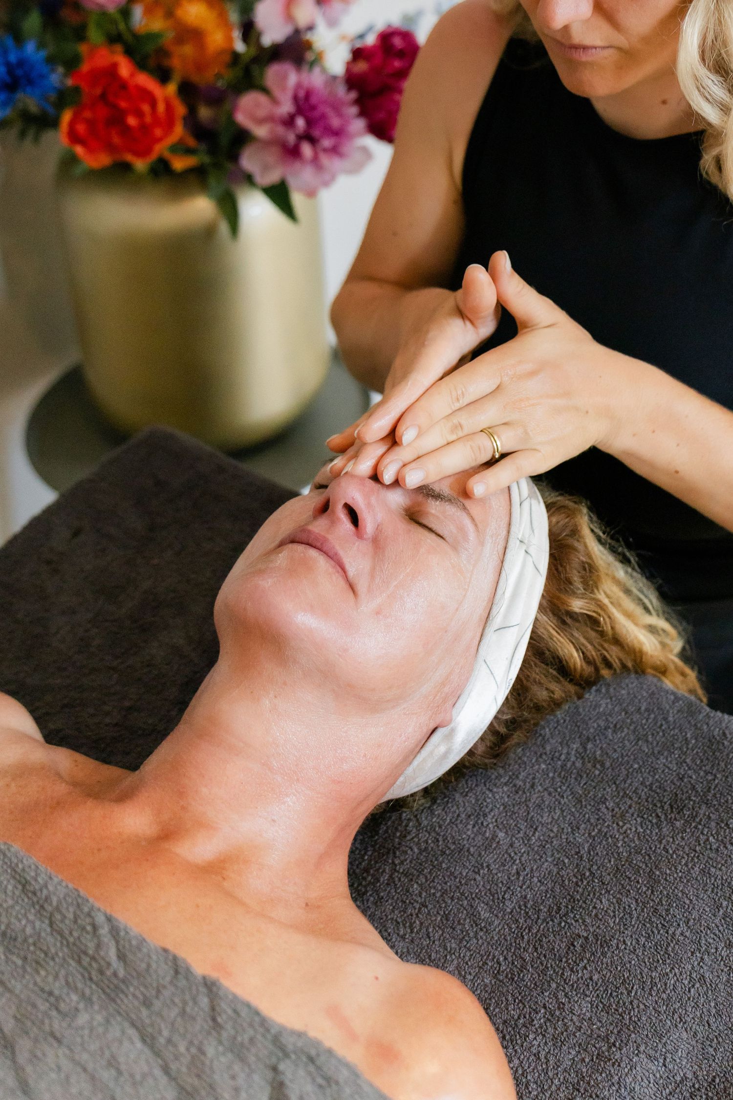 A therapist performs a relaxing facial massage on a woman lying on a spa treatment table.