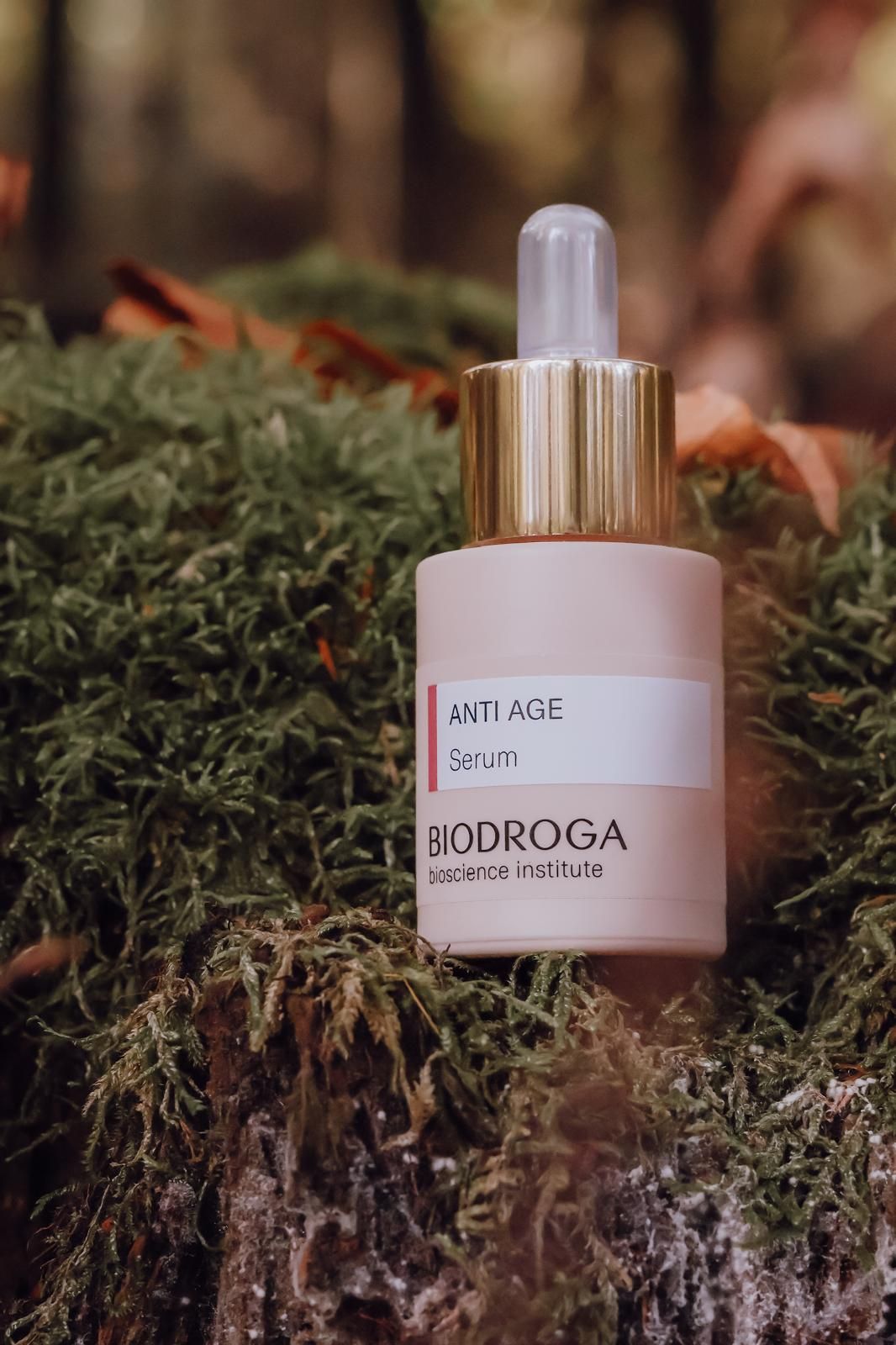 Biodroga Bioscience Institute Anti Age Serum bottle with gold dropper cap resting on green moss in a forest setting.
