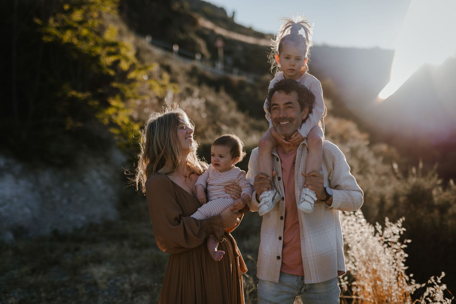 Joyful family with baby and toddler smiling in golden sunlight outdoors.