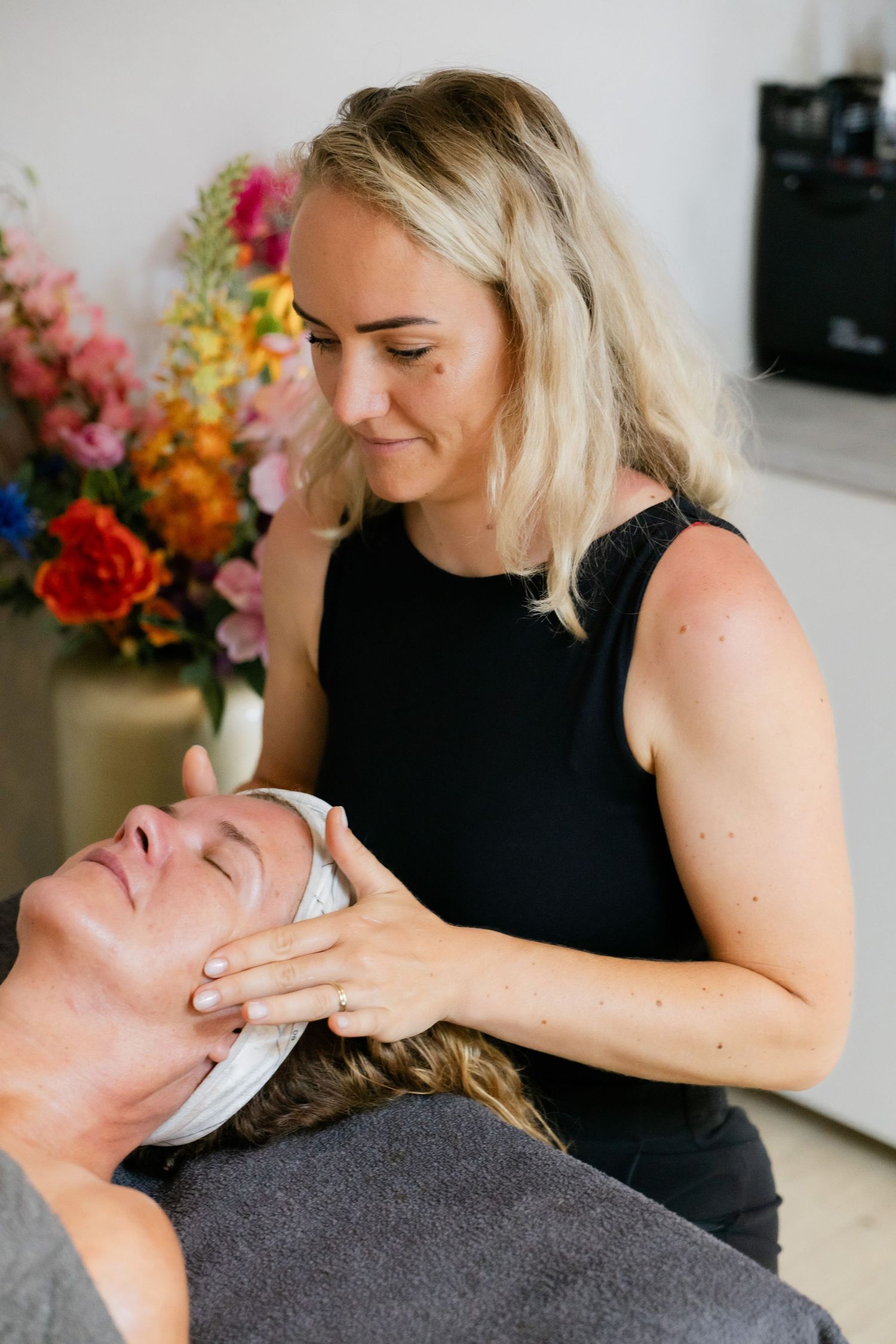 Blonde vrouwelijke schoonheidsspecialiste geeft een ontspannende gezichtsmassage aan een klant in een schoonheidssalon.