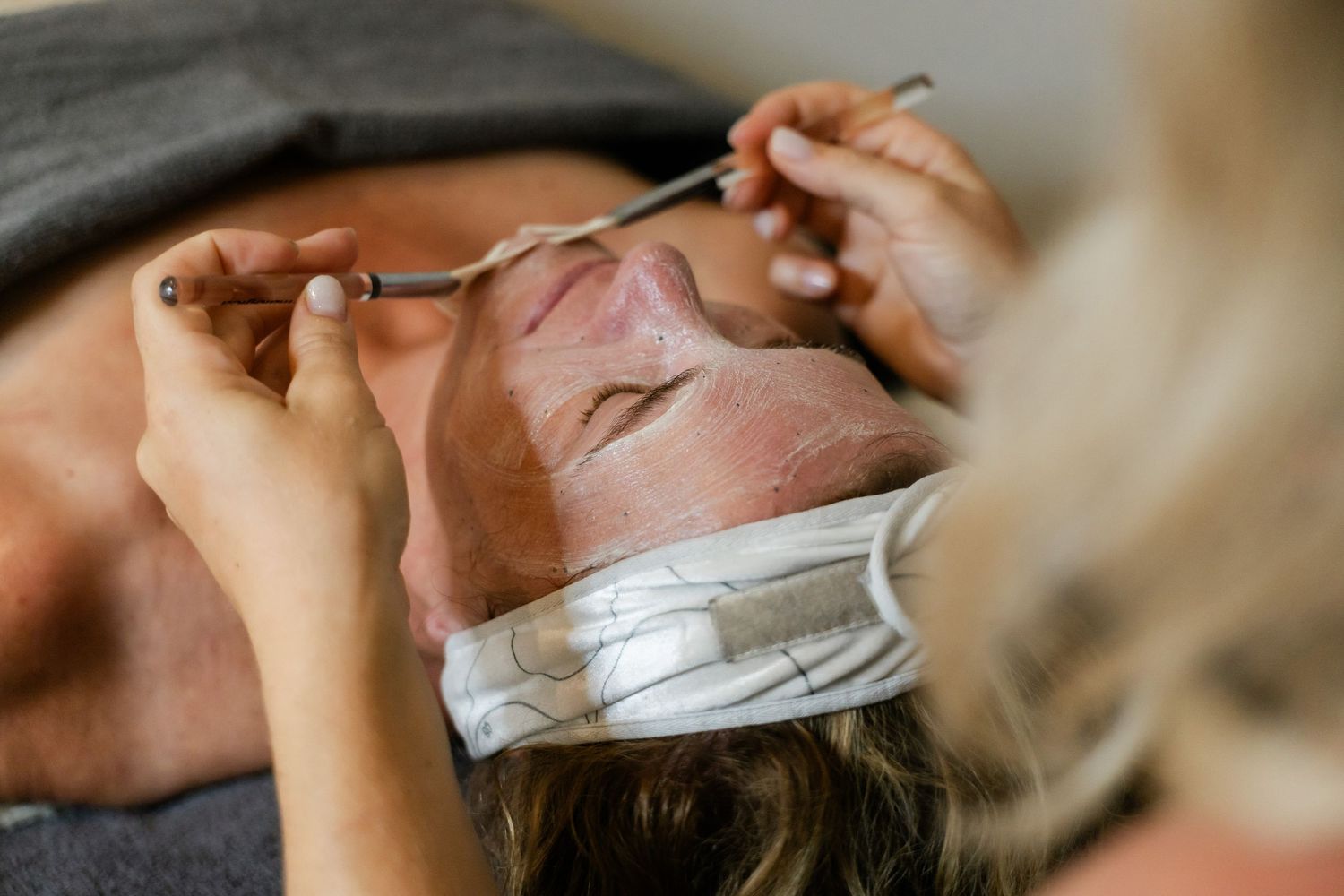 Professional esthetician performing facial treatment on client with pink clay mask in spa setting.