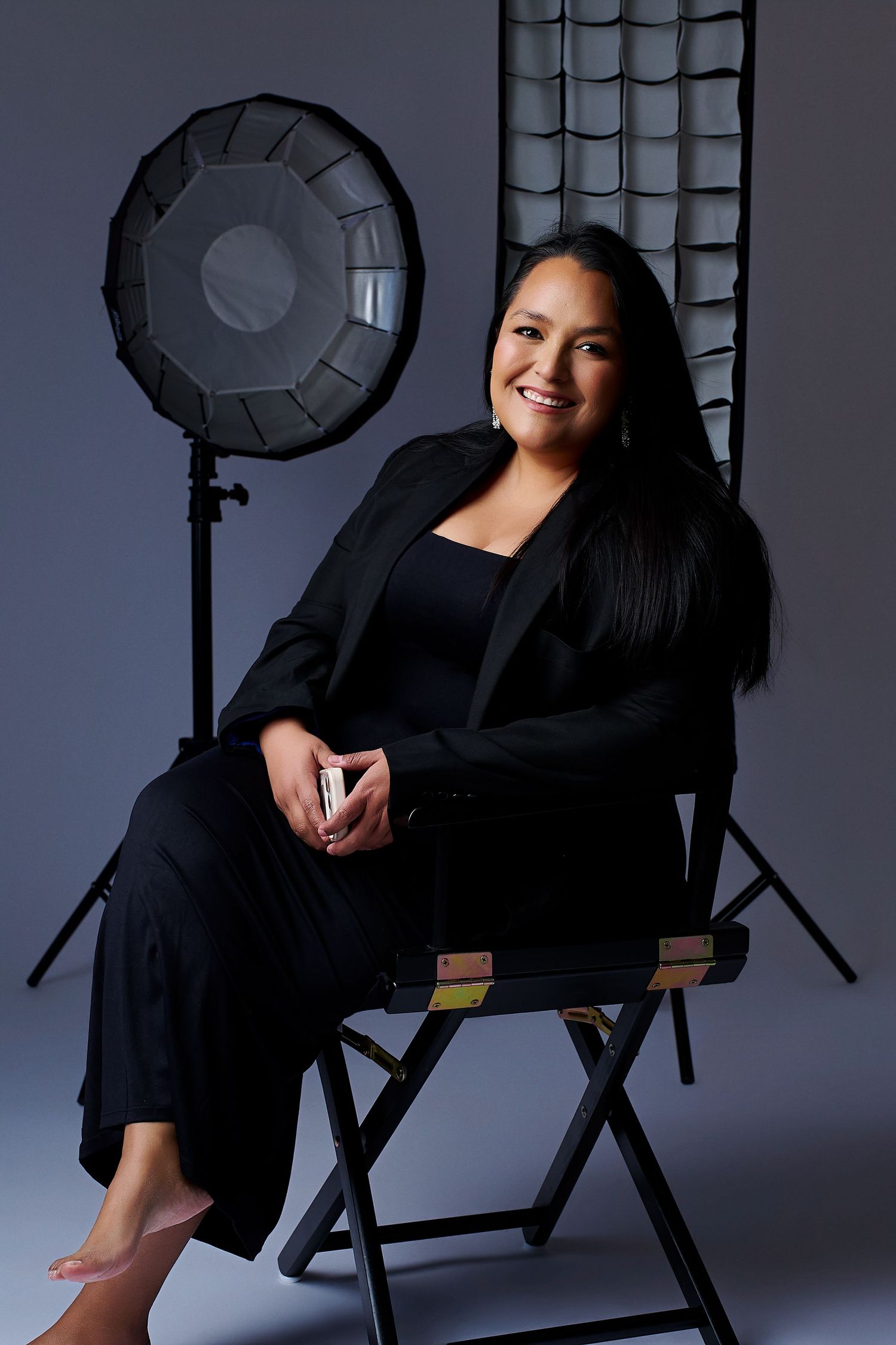 Professional studio portrait series showing a person in black clothing posing on a director's chair with lighting equipment.