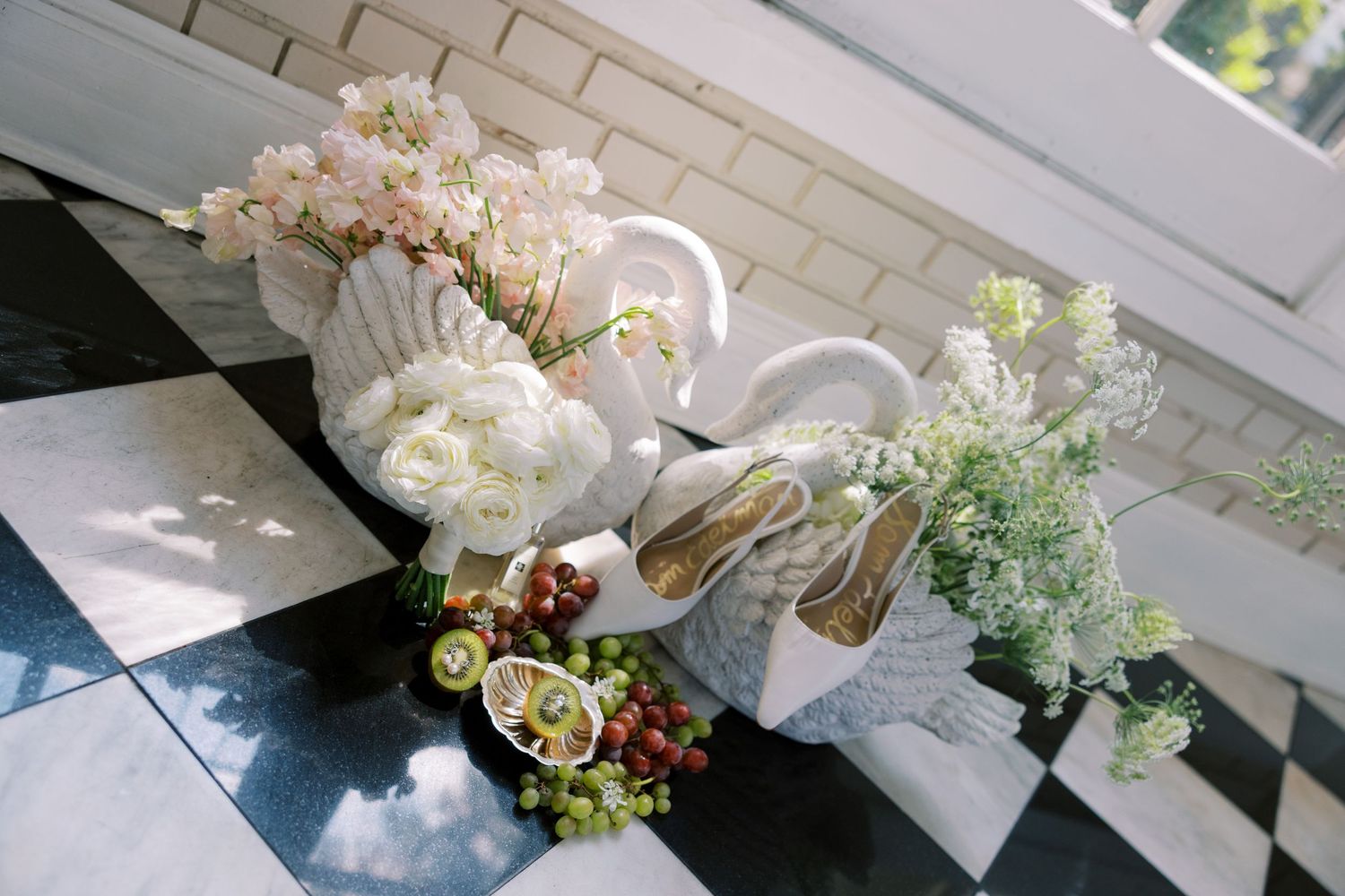 White wicker baskets with flowers, grapes, kiwi, and heels on black and white checkered floor.
