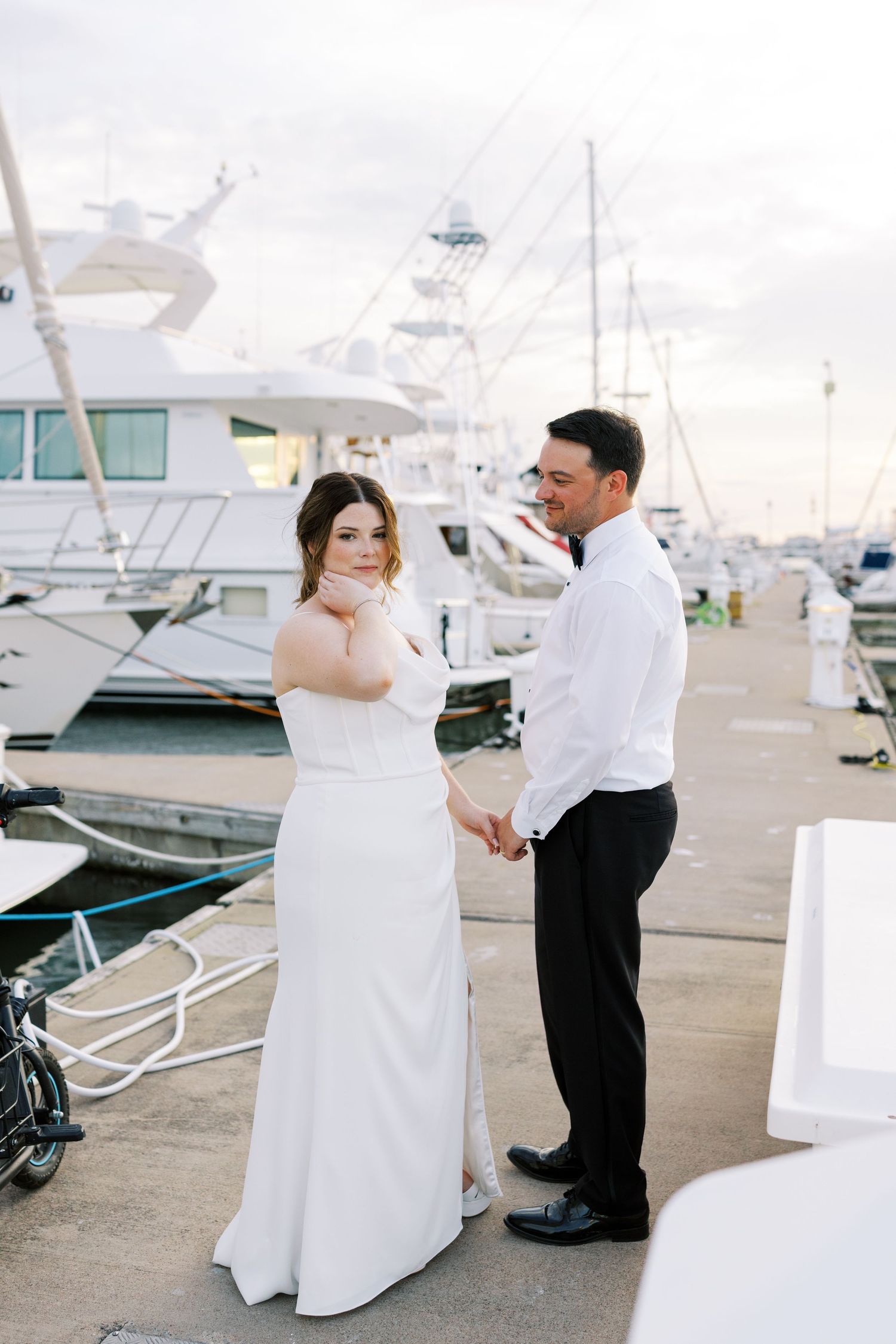 A couple shares a romantic dance moment together on a marina dock with boats in the background.