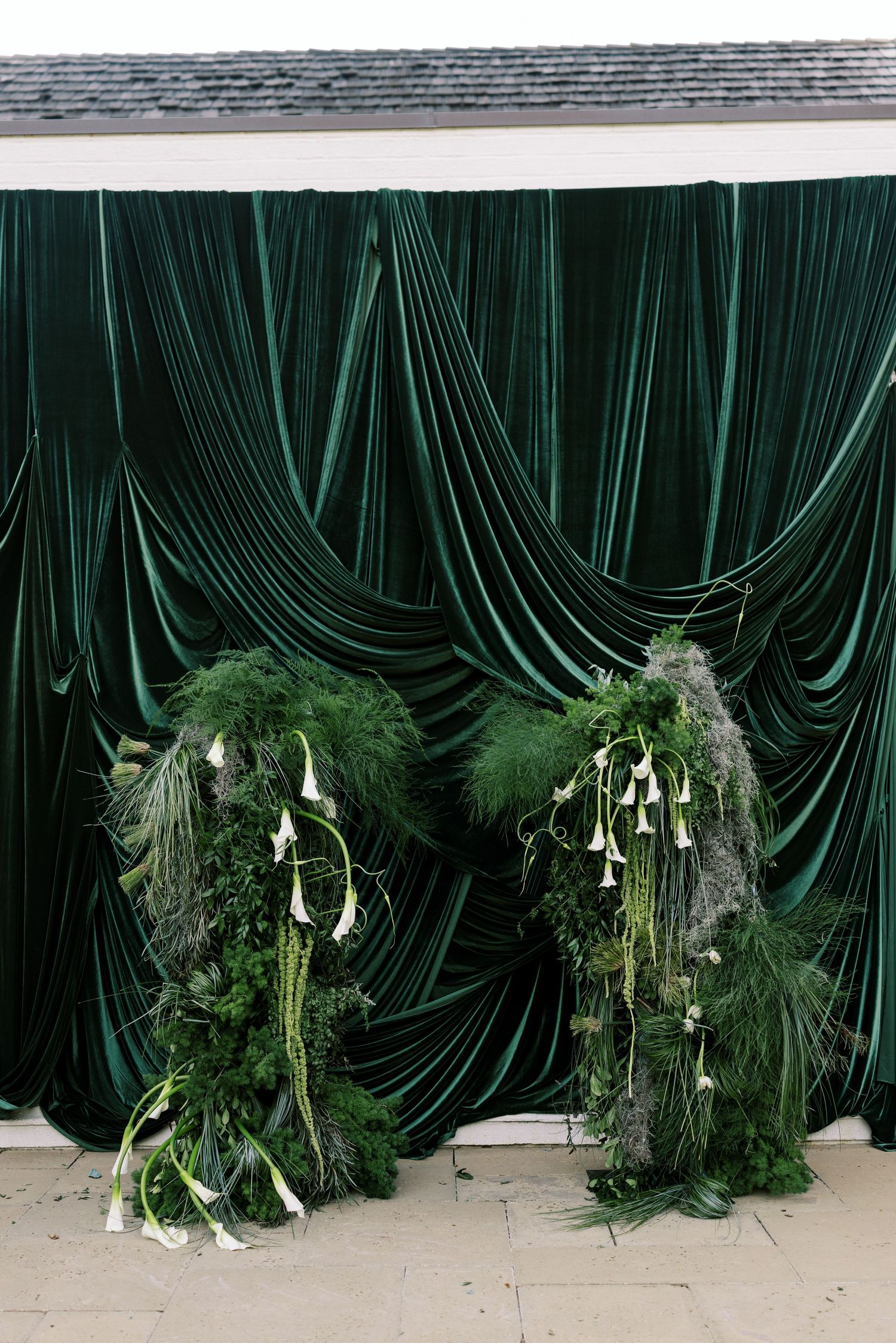 A sequence of dark green velvet curtains with cascading white calla lilies and greenery arrangements at the base.
