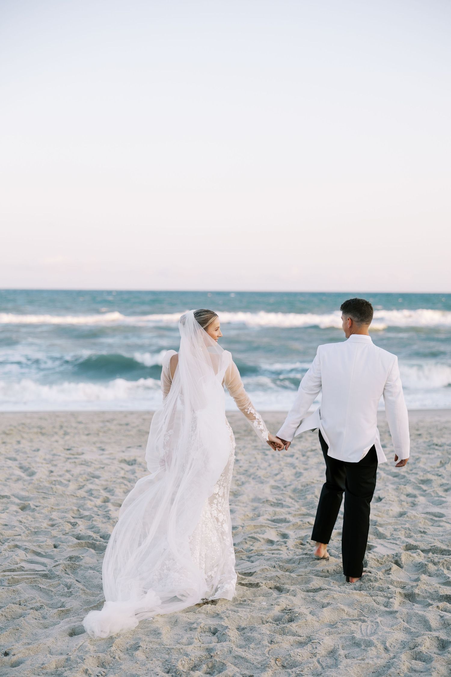 Couple walking hand in hand on beach with flowing white wedding dress. luxury wedding photographer. north carolina wedding photographer.