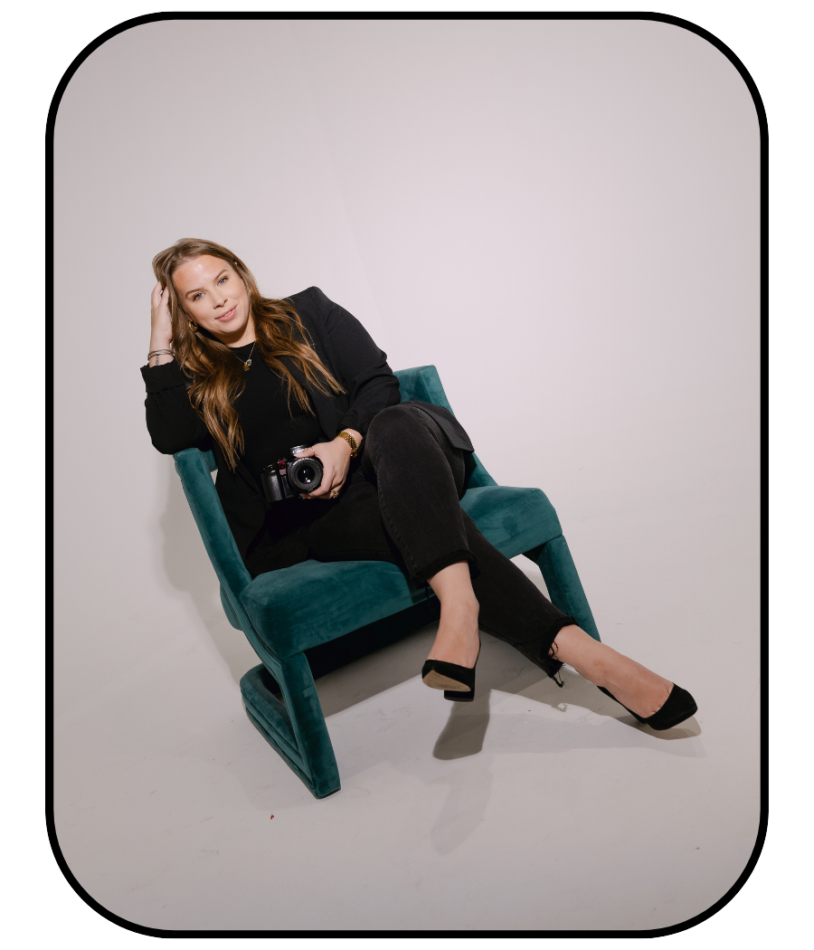 A person in black clothing lounges on a teal velvet armchair against a white backdrop in a minimalist setting.