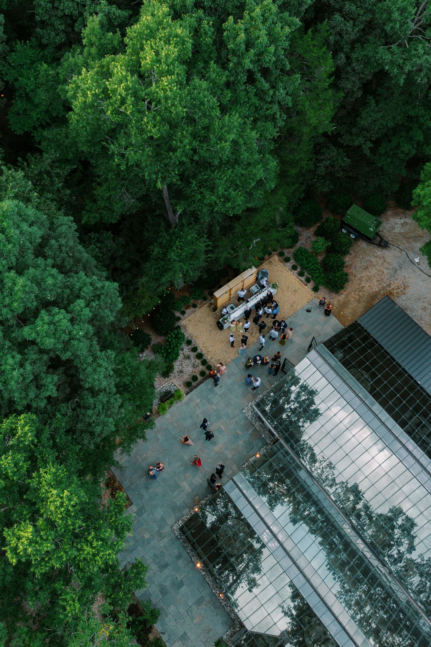 Aerial view of people gathering near a food truck surrounded by lush green trees and a glass building.