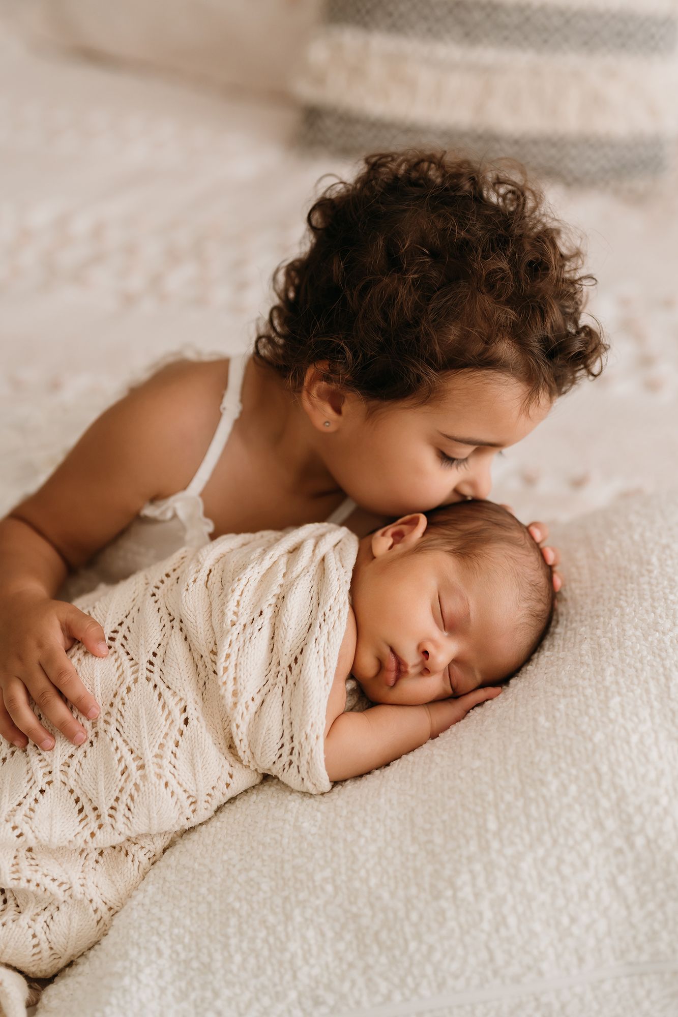 Older sibling gently kissing their newborn baby at home