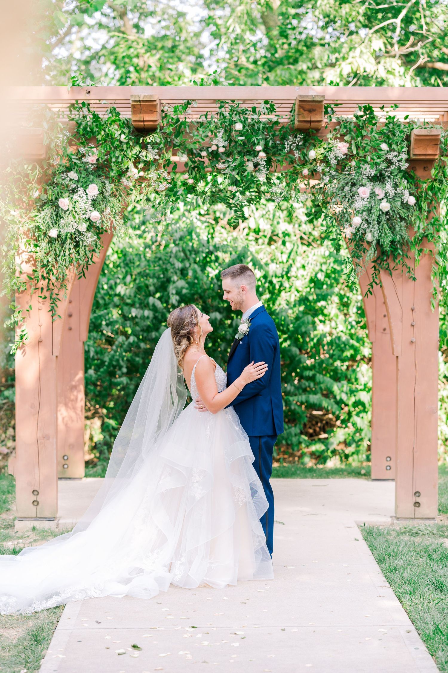 Bride and Groom standing together in front of an arbor surrounded by greenery and flowers