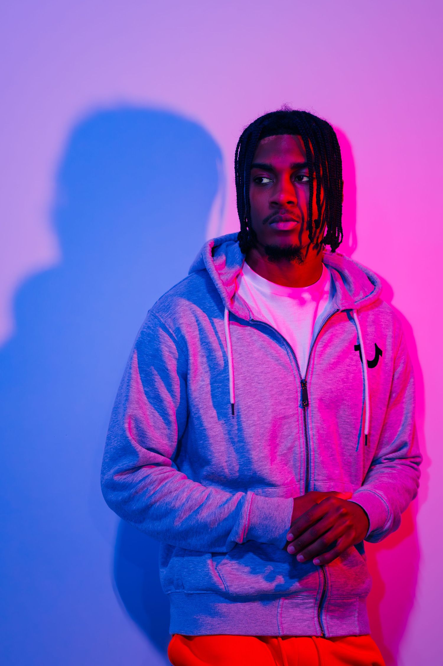 editorial creative photo using pink light and shadow featuring black man with braids and a hoodie