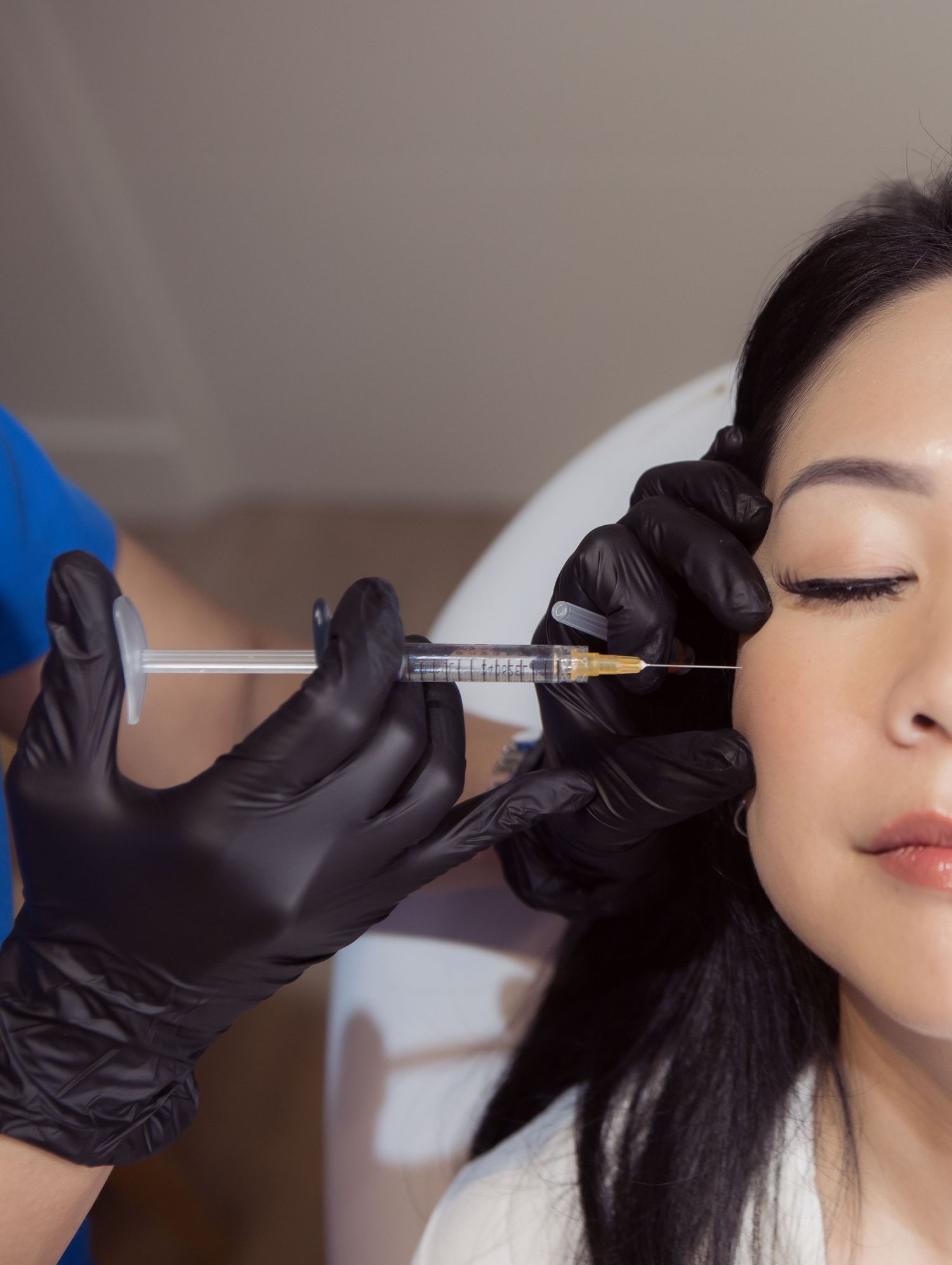 Medical professional wearing black gloves administers injectable treatment to patient during cosmetic procedure.