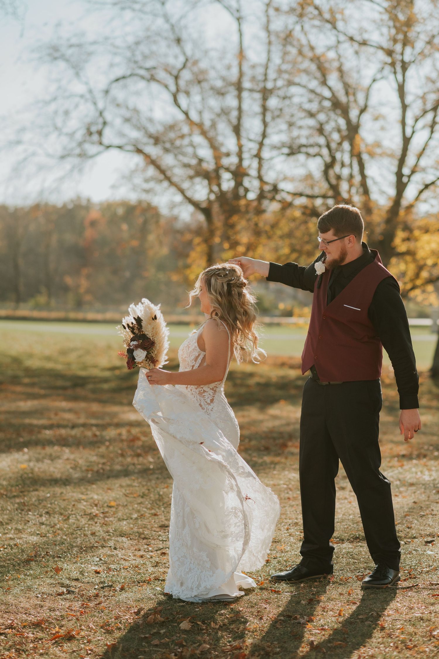 Bride and groom dancing outdoors among autumn foliage in warm golden sunlight.
