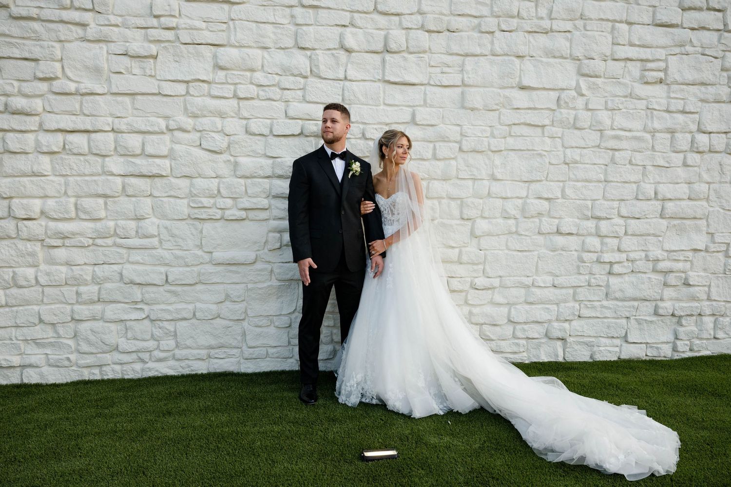 Bride and groom posing elegantly in front of a white brick wall on their wedding day.