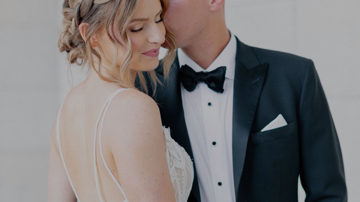 Close-up of bride and groom at wedding, showing elegant black tuxedo and white bridal gown details.