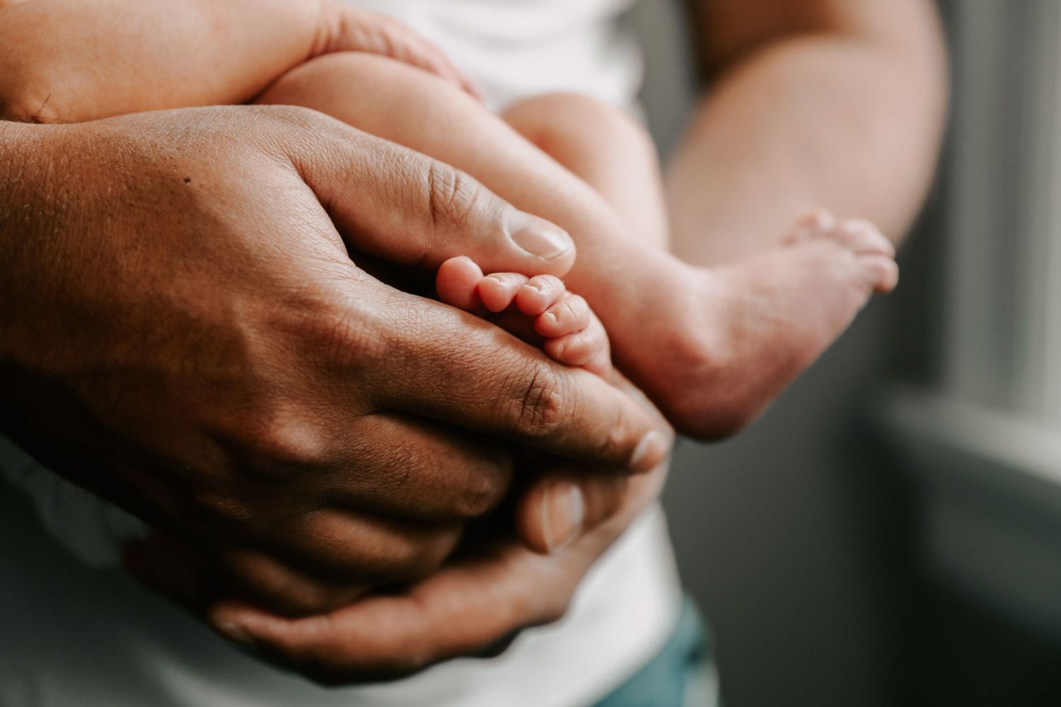 Close-up of tiny baby feet being held in adult hands near a window.