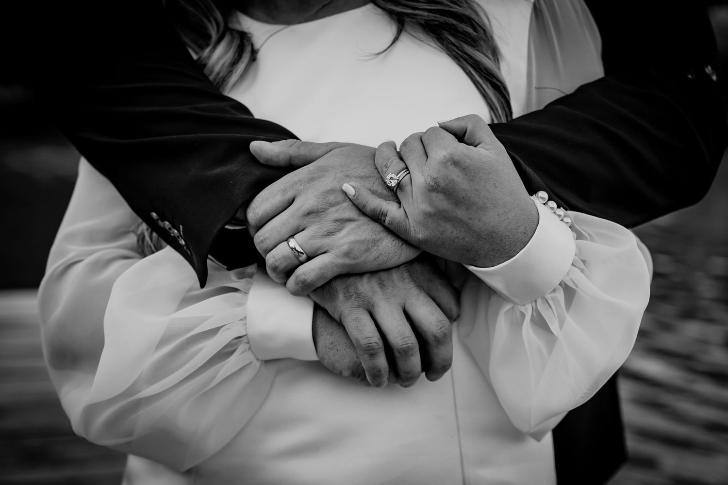 Close-up black and white photo of hands with wedding rings intertwined.