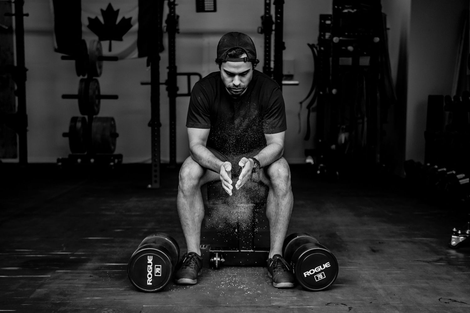 A weightlifter takes a rest between sets with heavy dumbbells in a dimly lit gym.