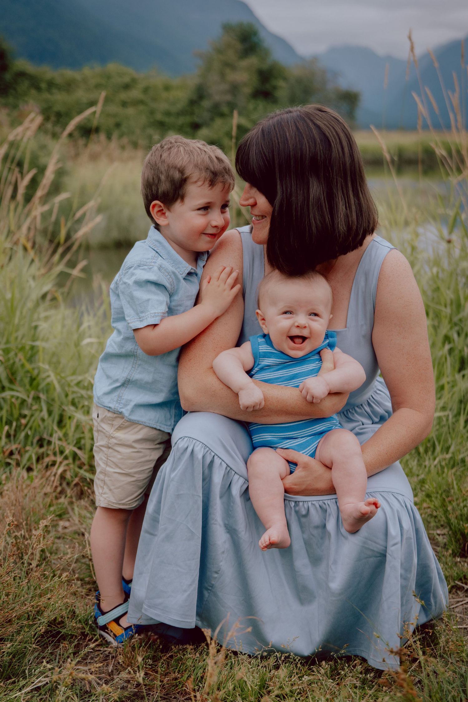 A joyful family moment captured outdoors with mountains and tall grass in the background.