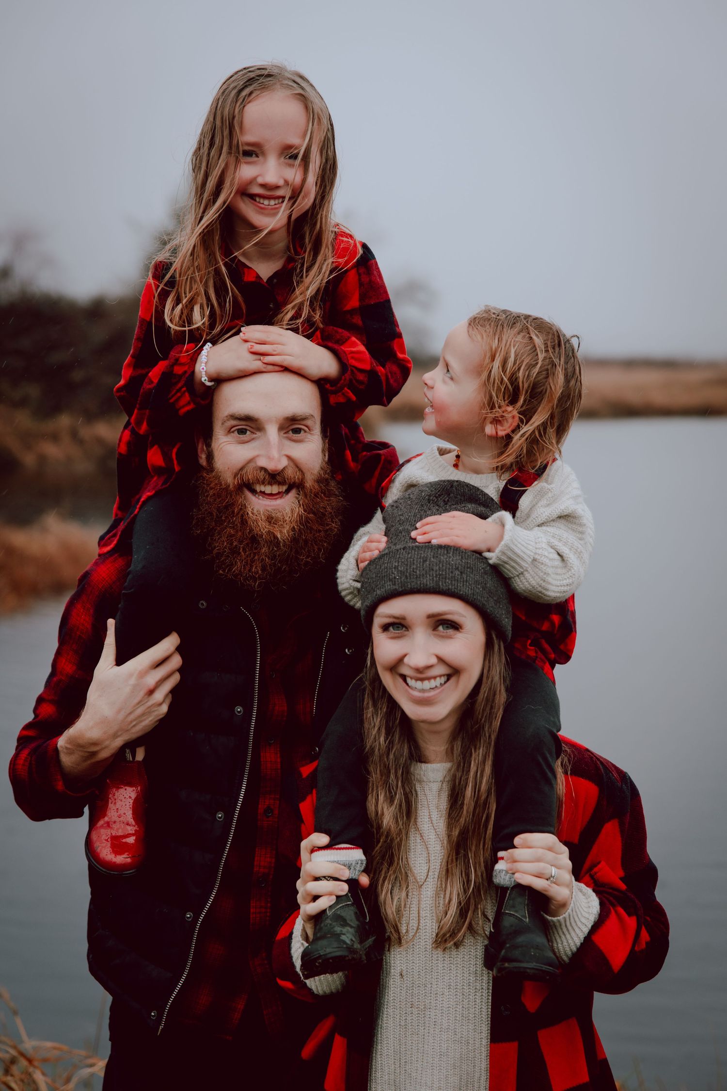 A family wearing matching buffalo plaid outfits poses playfully by a lake.