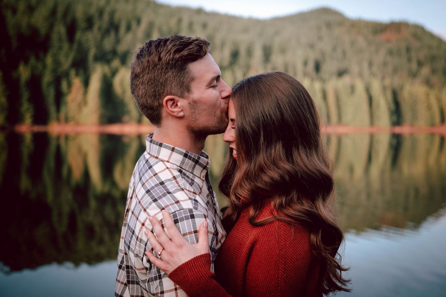Romantic lakeside moment with mountain and forest reflections in water.