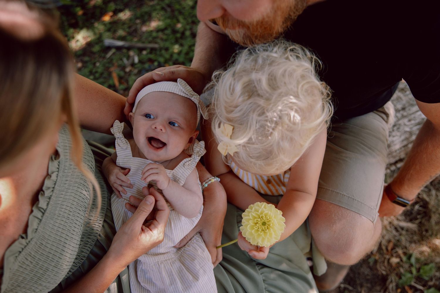 Laughing baby in white dress being held on a sunny summer day outdoors.