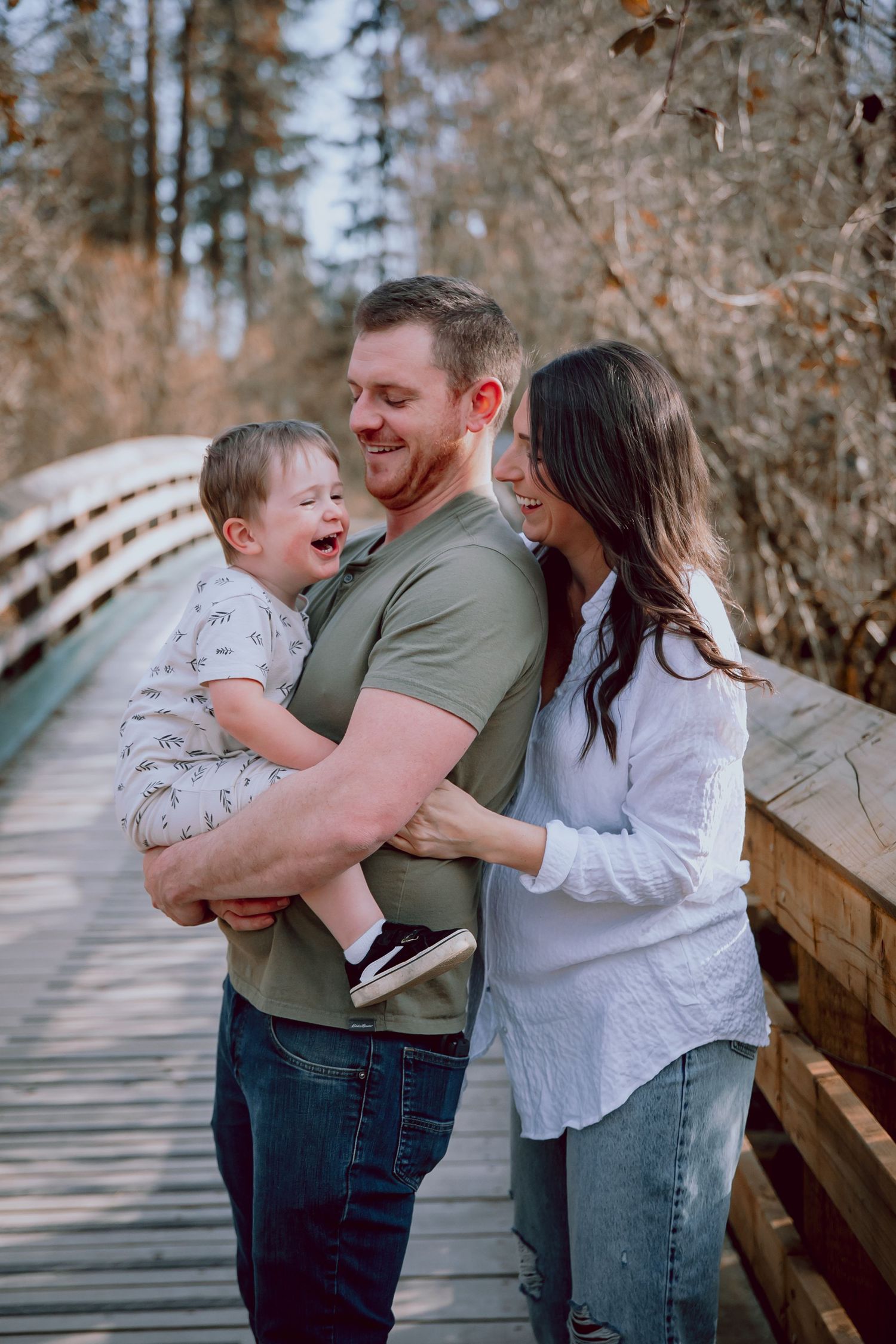 A family shares a candid laughing moment together on a wooden bridge in the forest.
