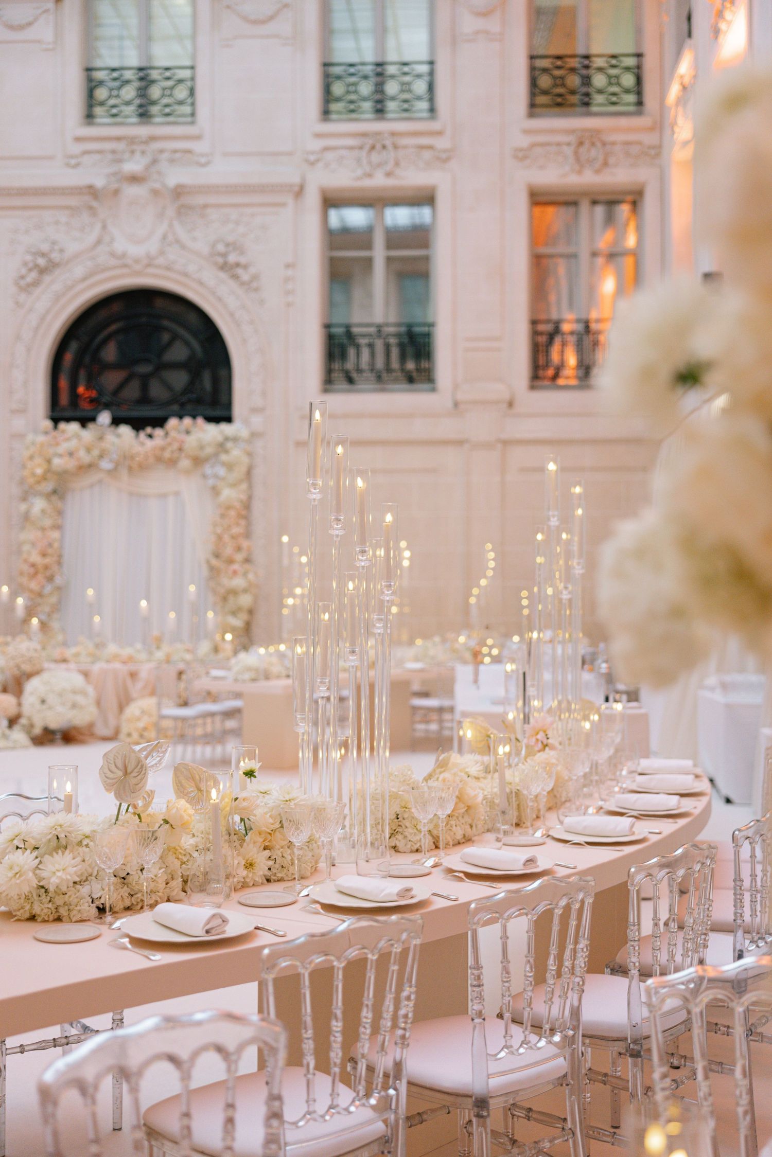Elegant white and gold wedding reception tables set with tall candles in a luxurious ballroom setting.