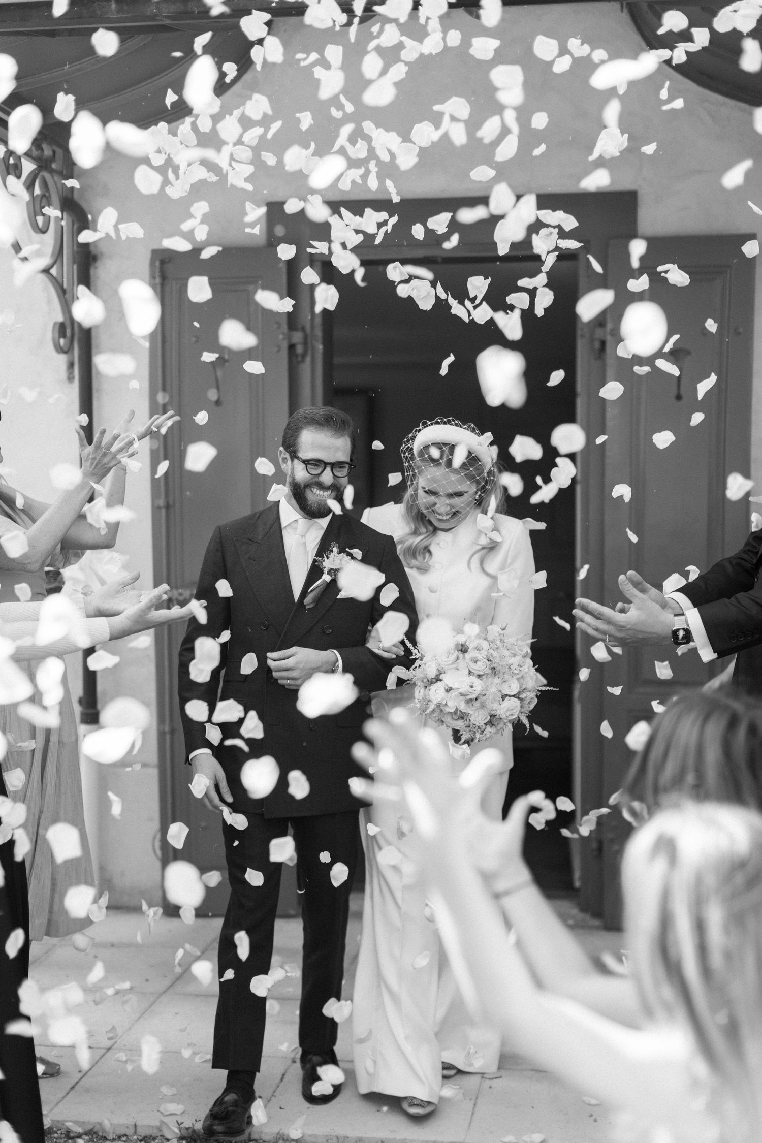 A joyful wedding celebration with white rose petals being tossed in the air during a reception entrance.