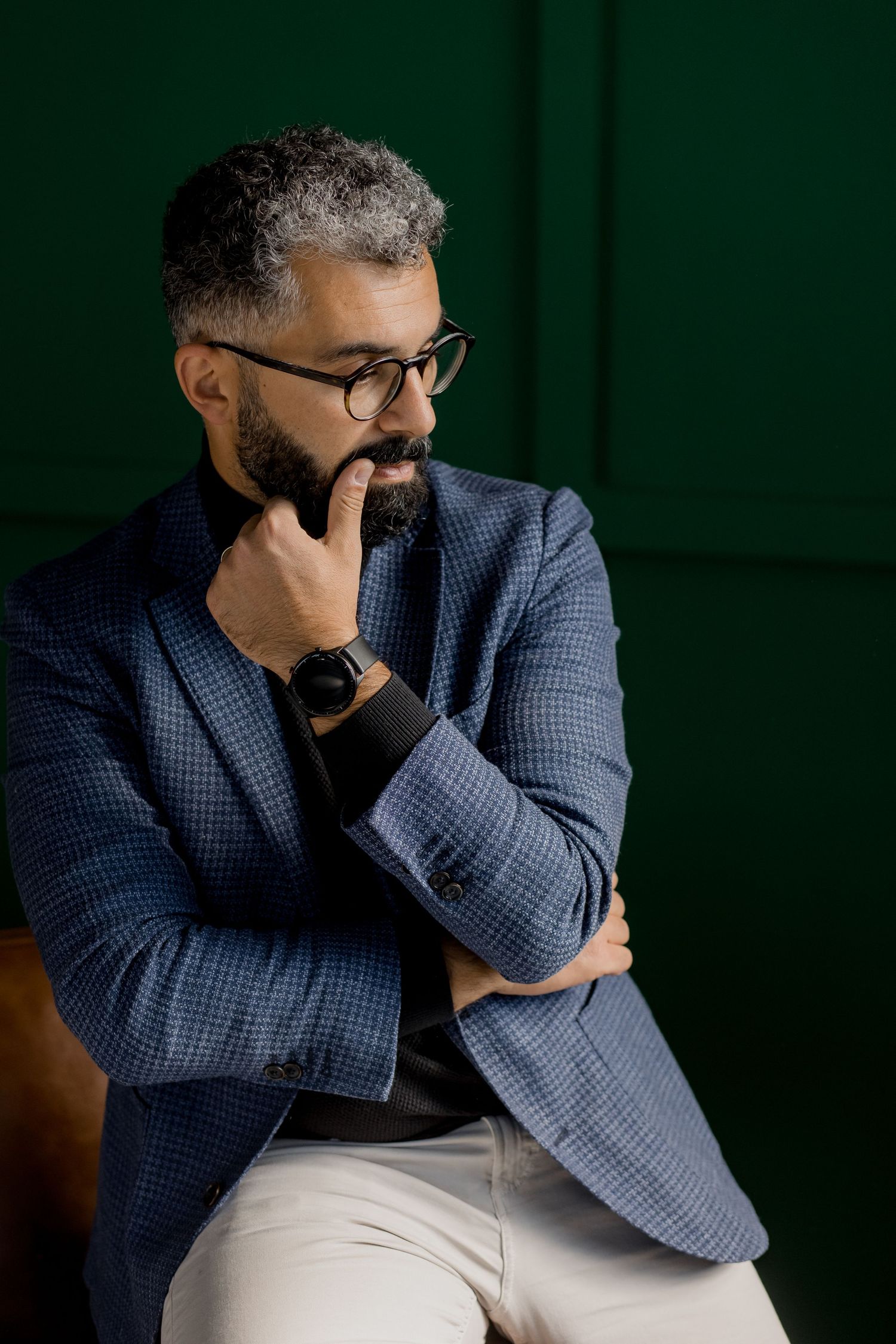 Professional in blue checkered blazer sits thoughtfully against dark green background.